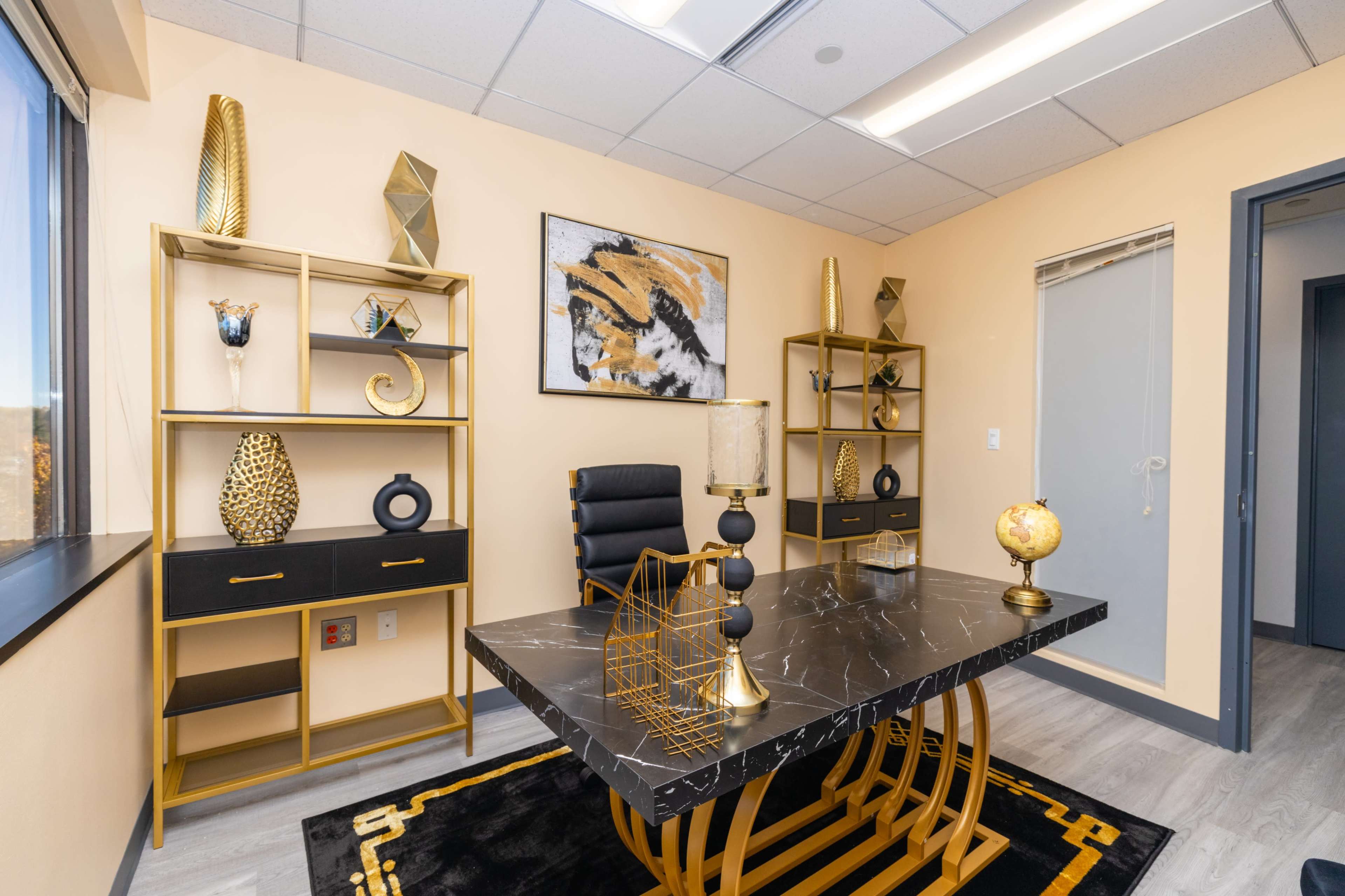A modern office with a black marble desk, gold accents, and decorative shelves featuring geometric objects and a globe.