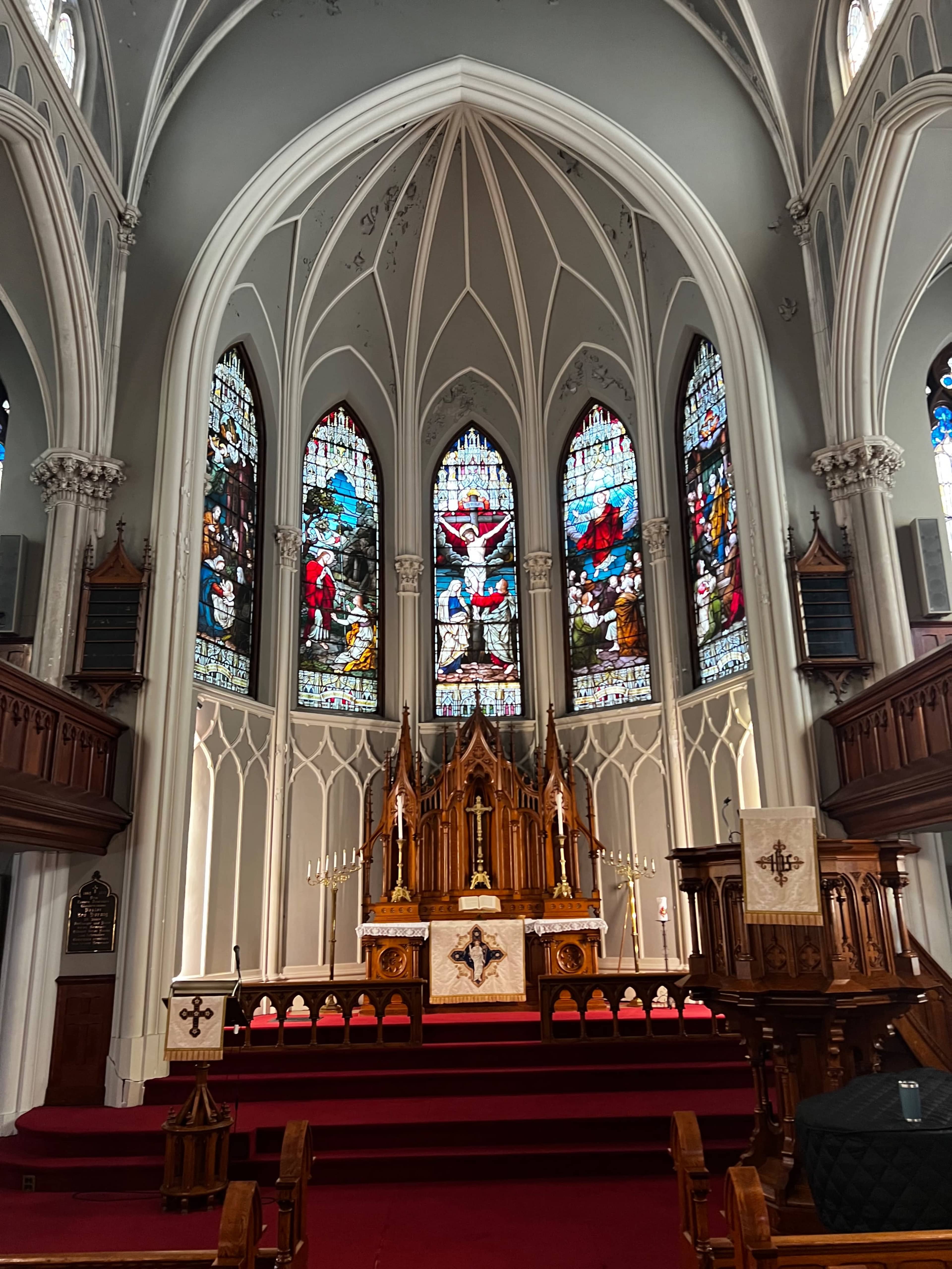 The image shows the interior of a church featuring an altar with elaborate woodwork and stained glass windows depicting biblical scenes.