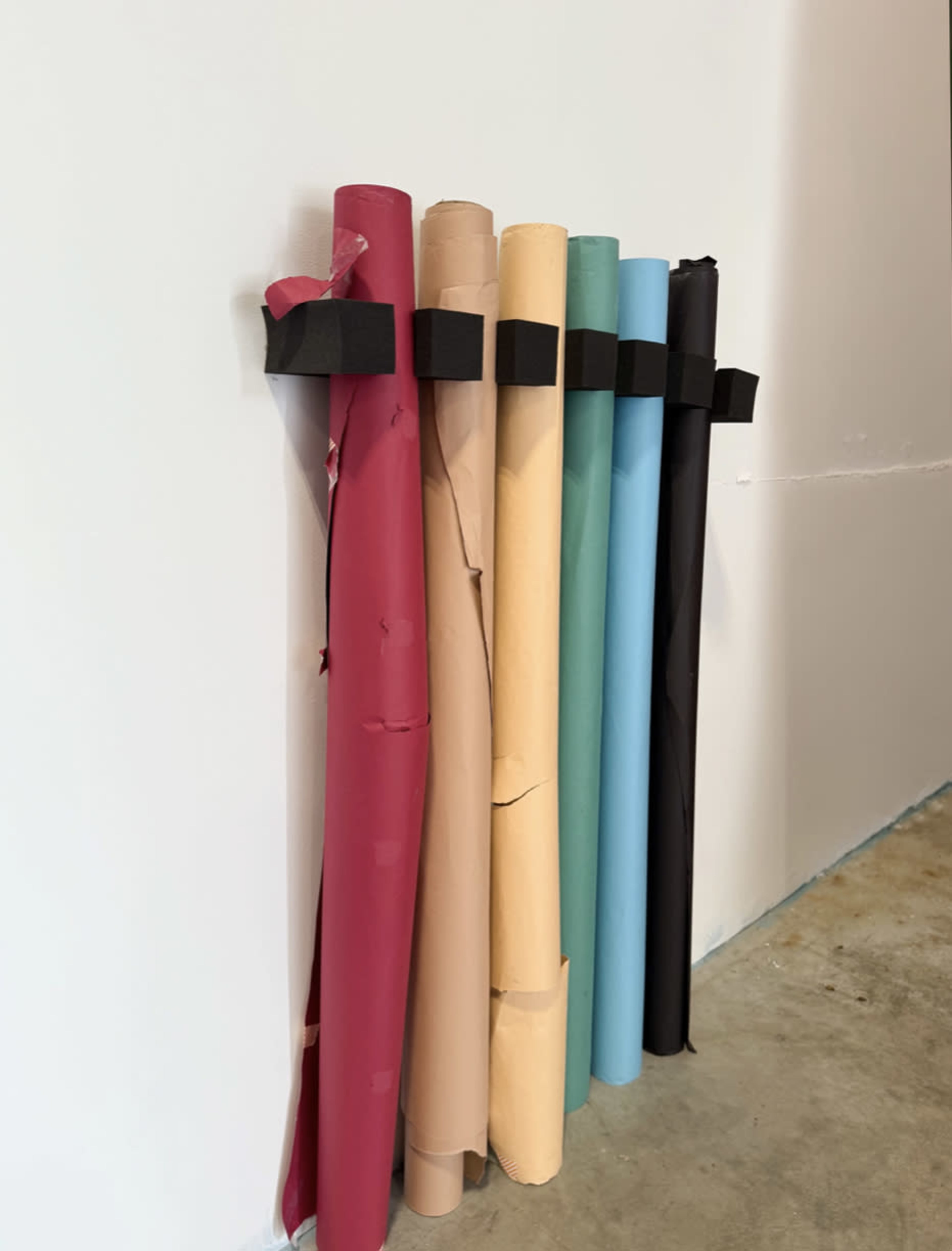 A collection of rolled paper in various colors is secured against a wall with black tape.