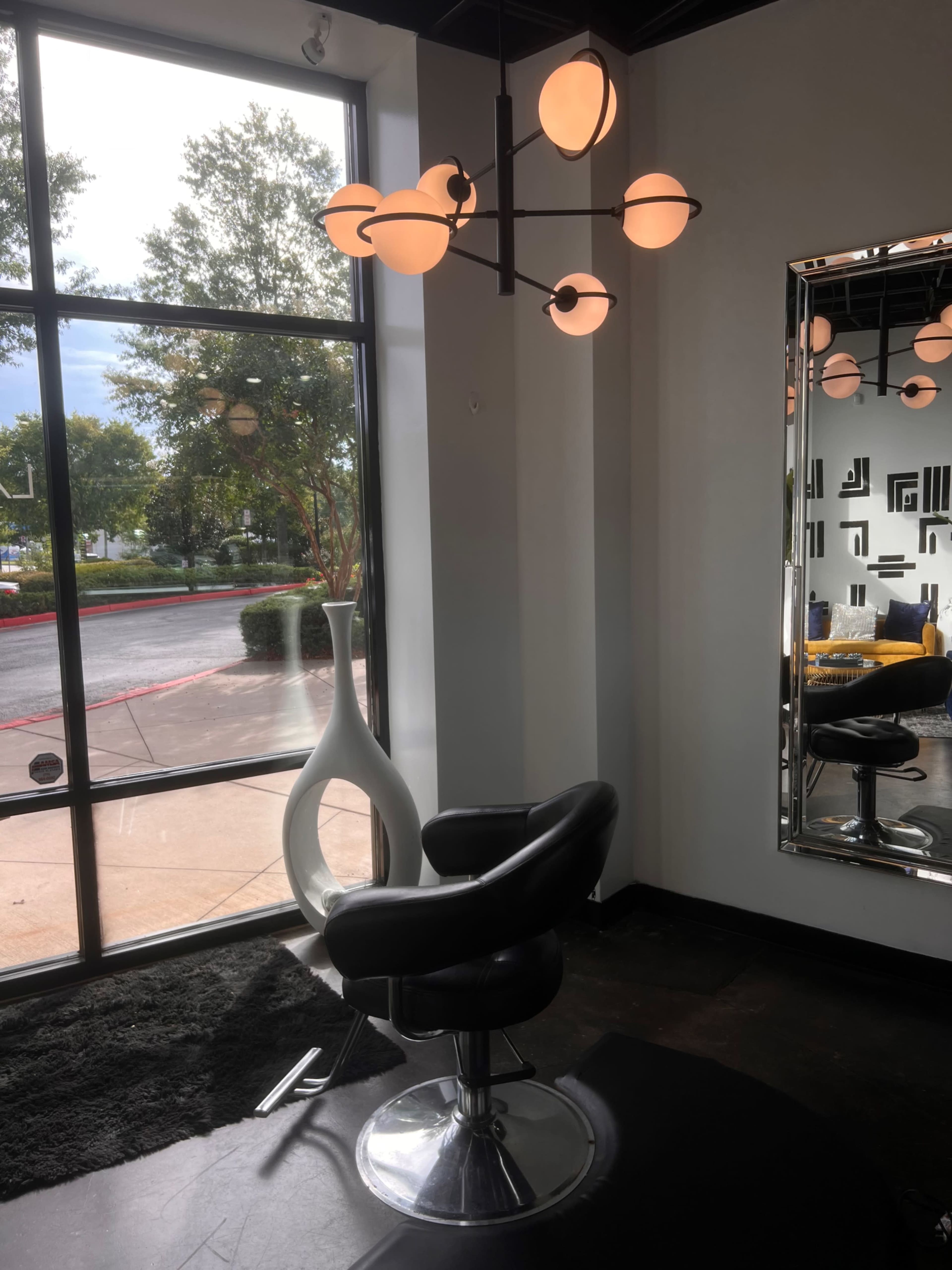 A modern salon interior with a black barber chair, a stylish lighting fixture, and a large mirror reflecting the space.