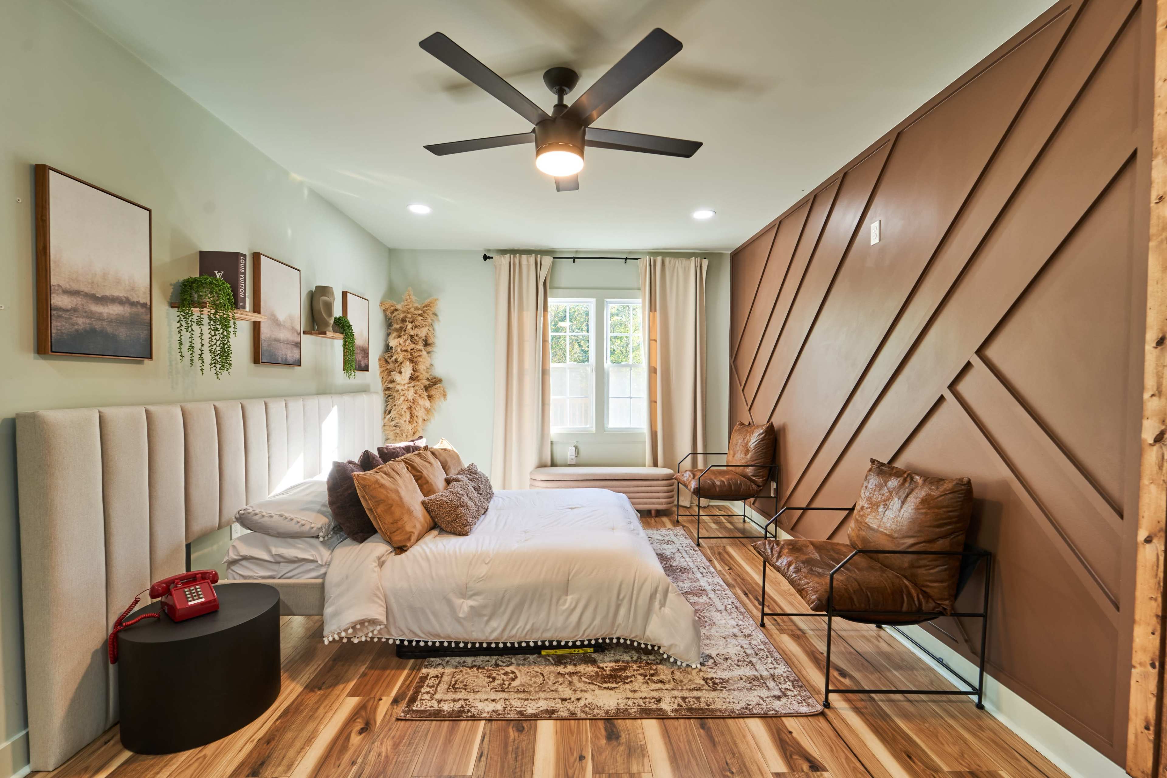 A modern bedroom with a bed, two leather chairs, and a decorative wall featuring geometric patterns.