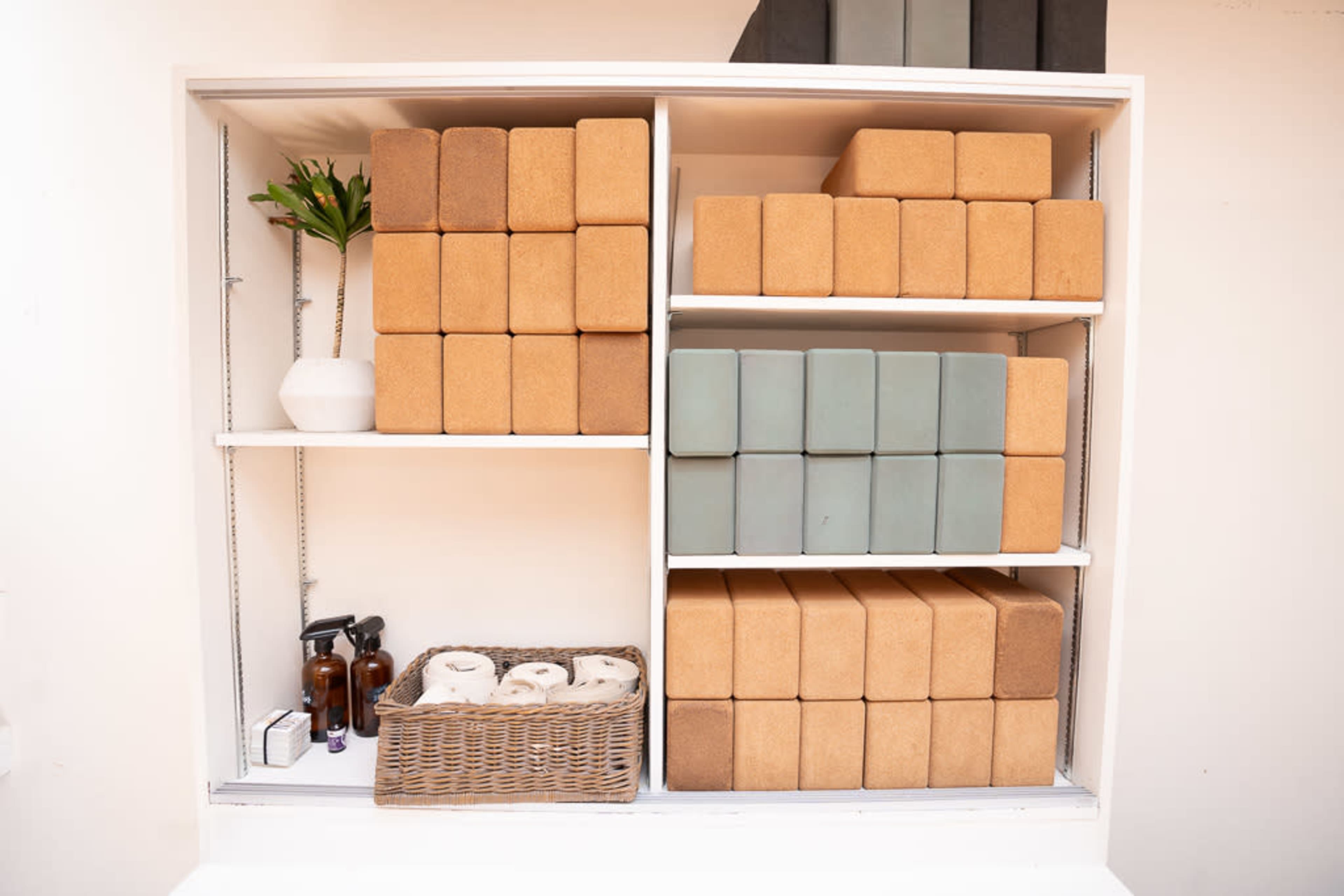 A shelf displays neatly stacked blocks in various colors alongside a basket of rolled towels and several bottles.