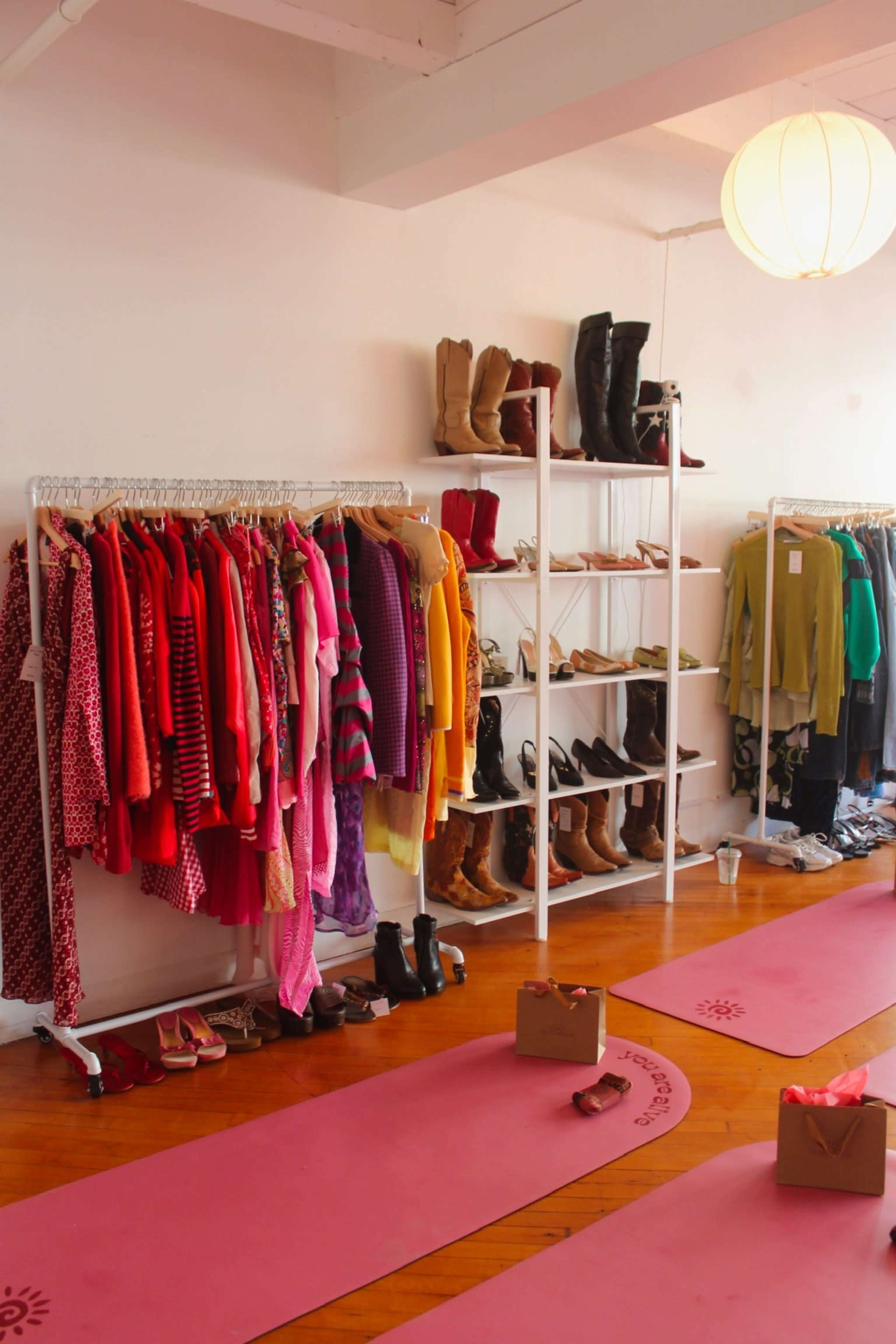 The image shows a brightly lit boutique with clothing racks displaying colorful garments and shelves lined with various boots and shoes on a wooden floor.