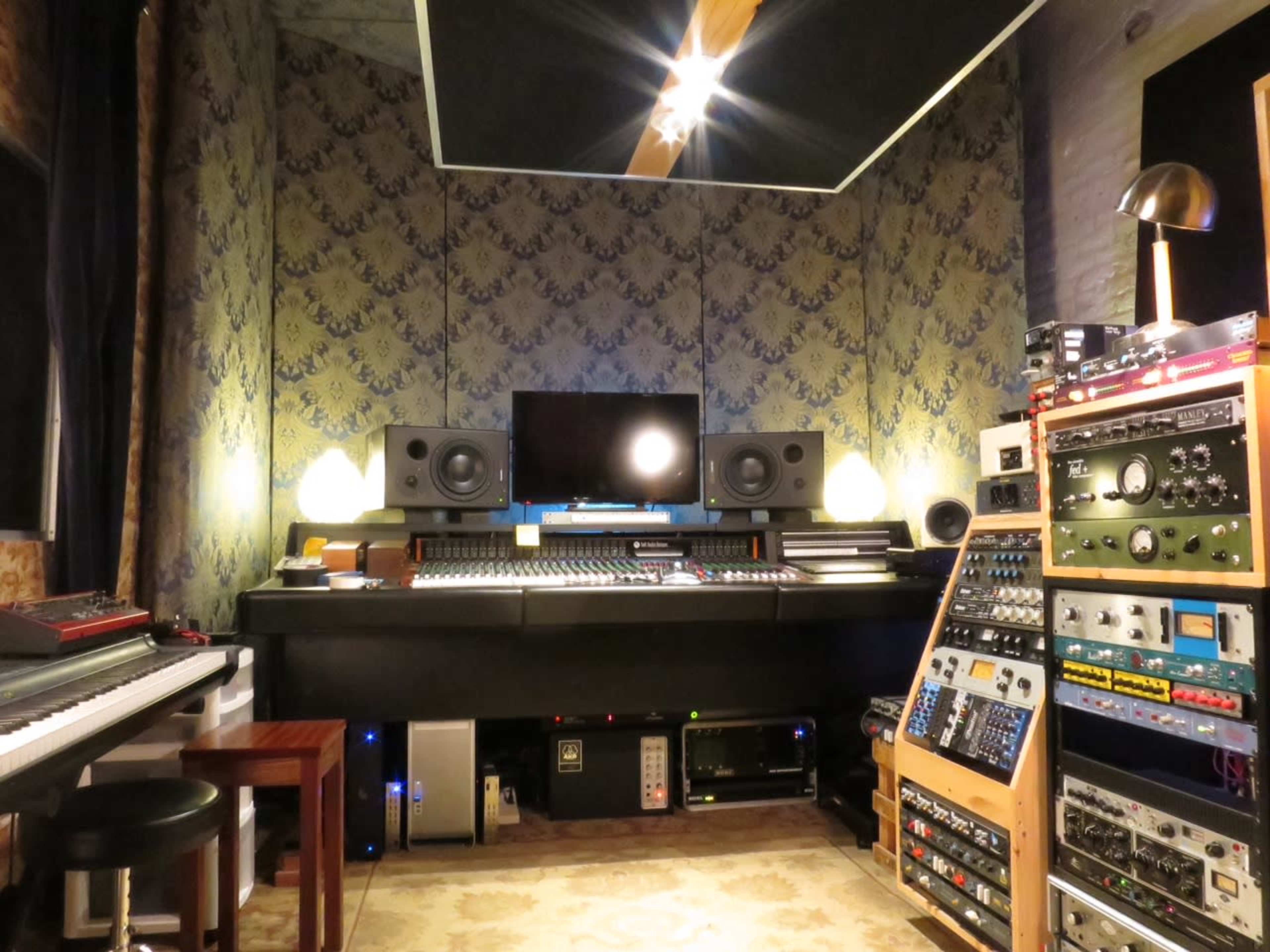A music studio featuring a mixing console, large speakers, a computer monitor, and racks of audio equipment.