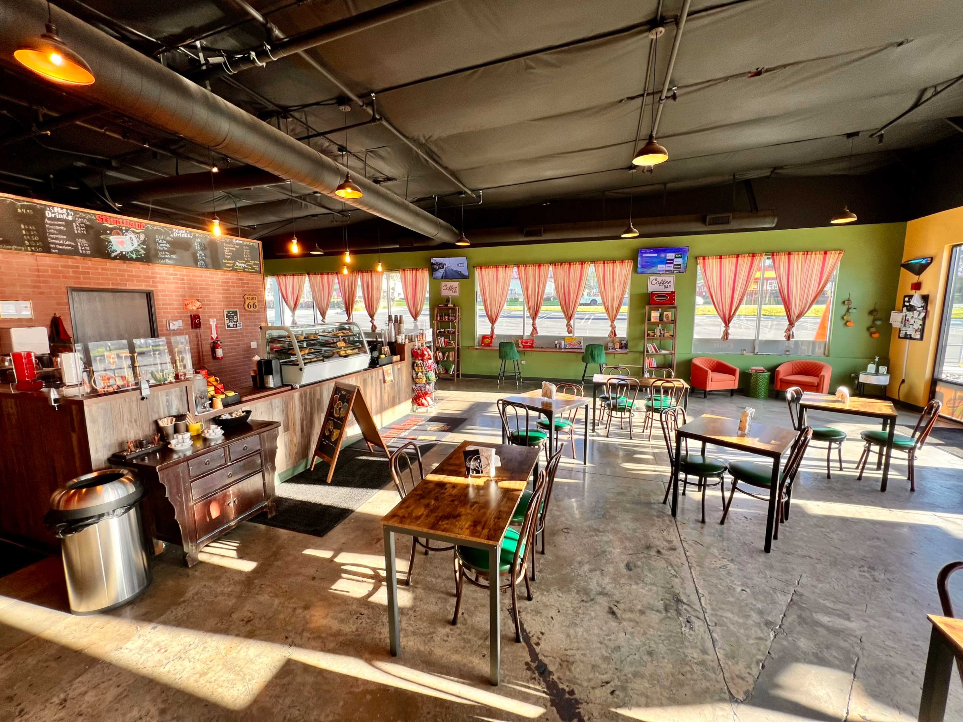 A spacious café with wooden tables, chairs, a service counter, and large windows adorned with curtains.