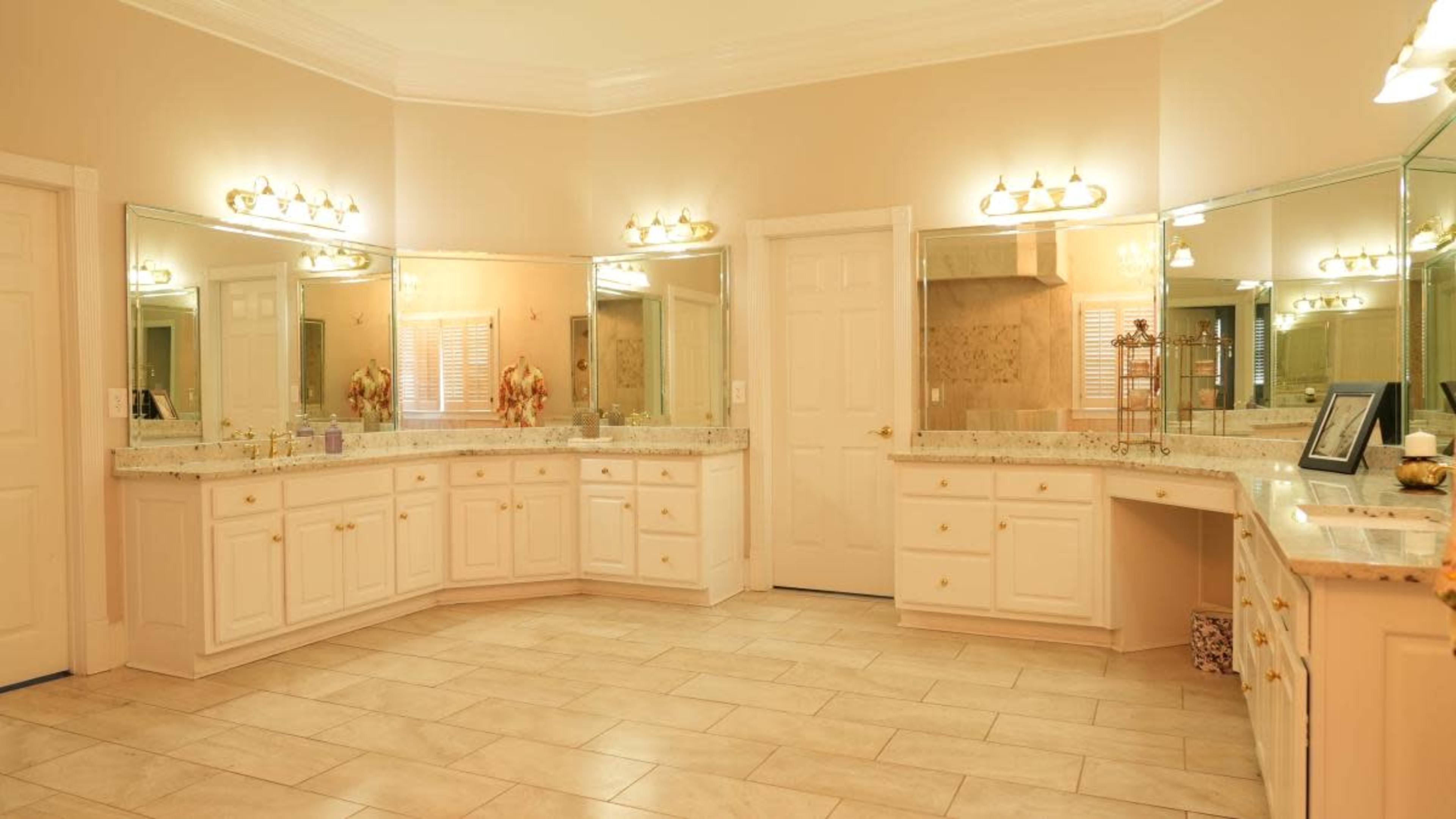 The image shows a spacious bathroom with dual vanities, large mirrors, and tiled flooring in a neutral color scheme.