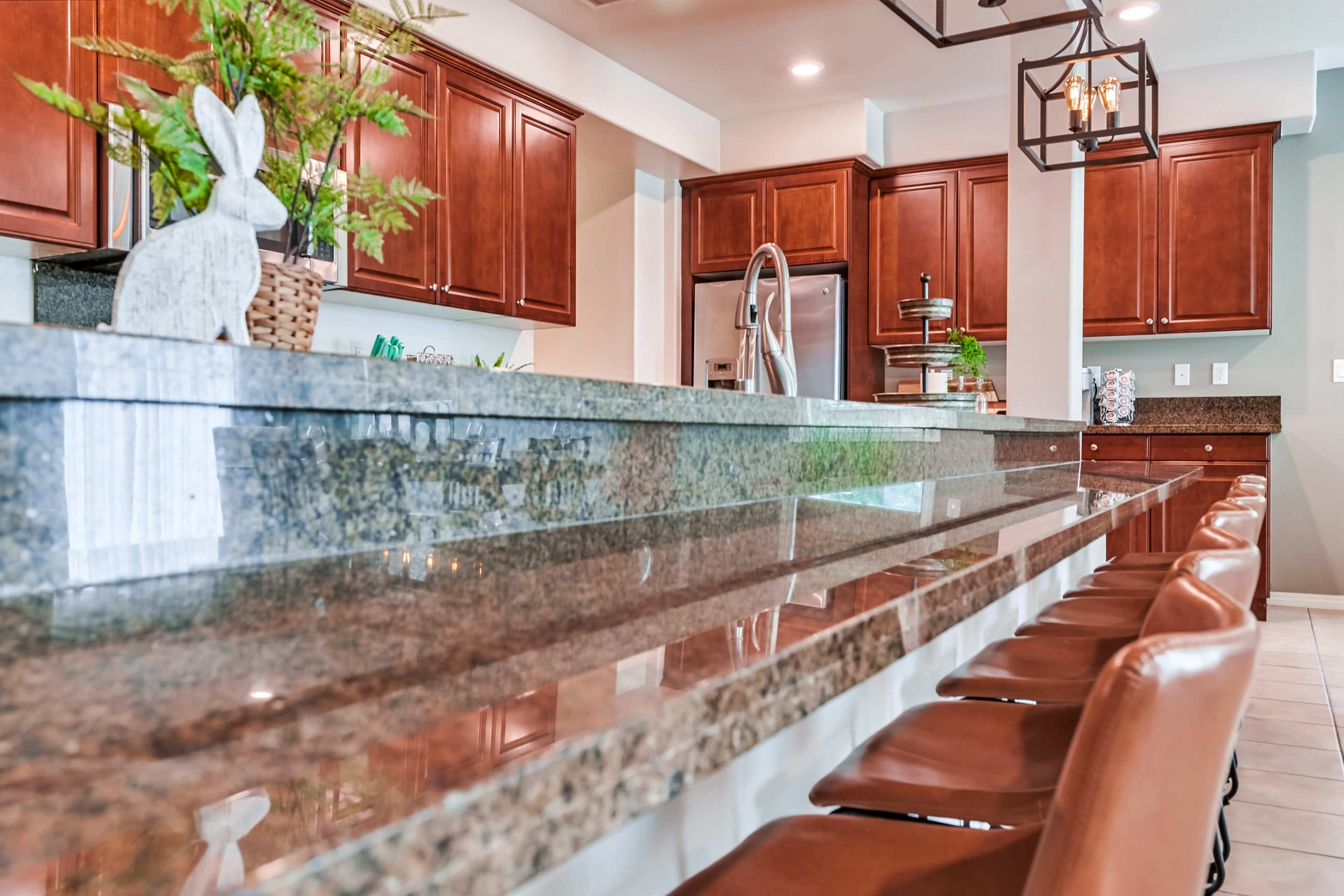 A modern kitchen with dark wooden cabinets, a large granite countertop with bar seating, and contemporary fixtures.