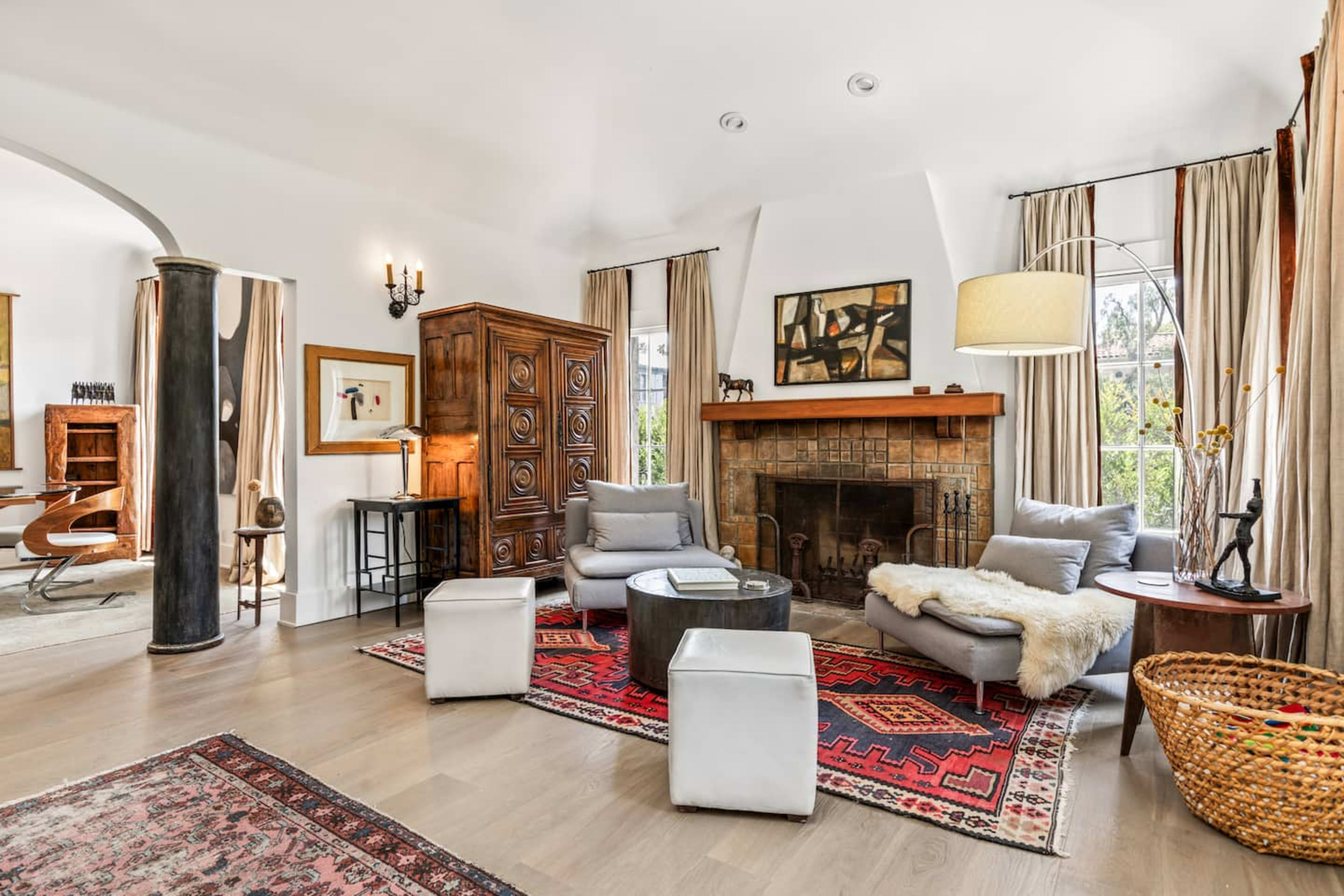 The image depicts a cozy living room featuring a fireplace, a wooden armoire, two gray sofas, and a circular coffee table on a patterned rug.
