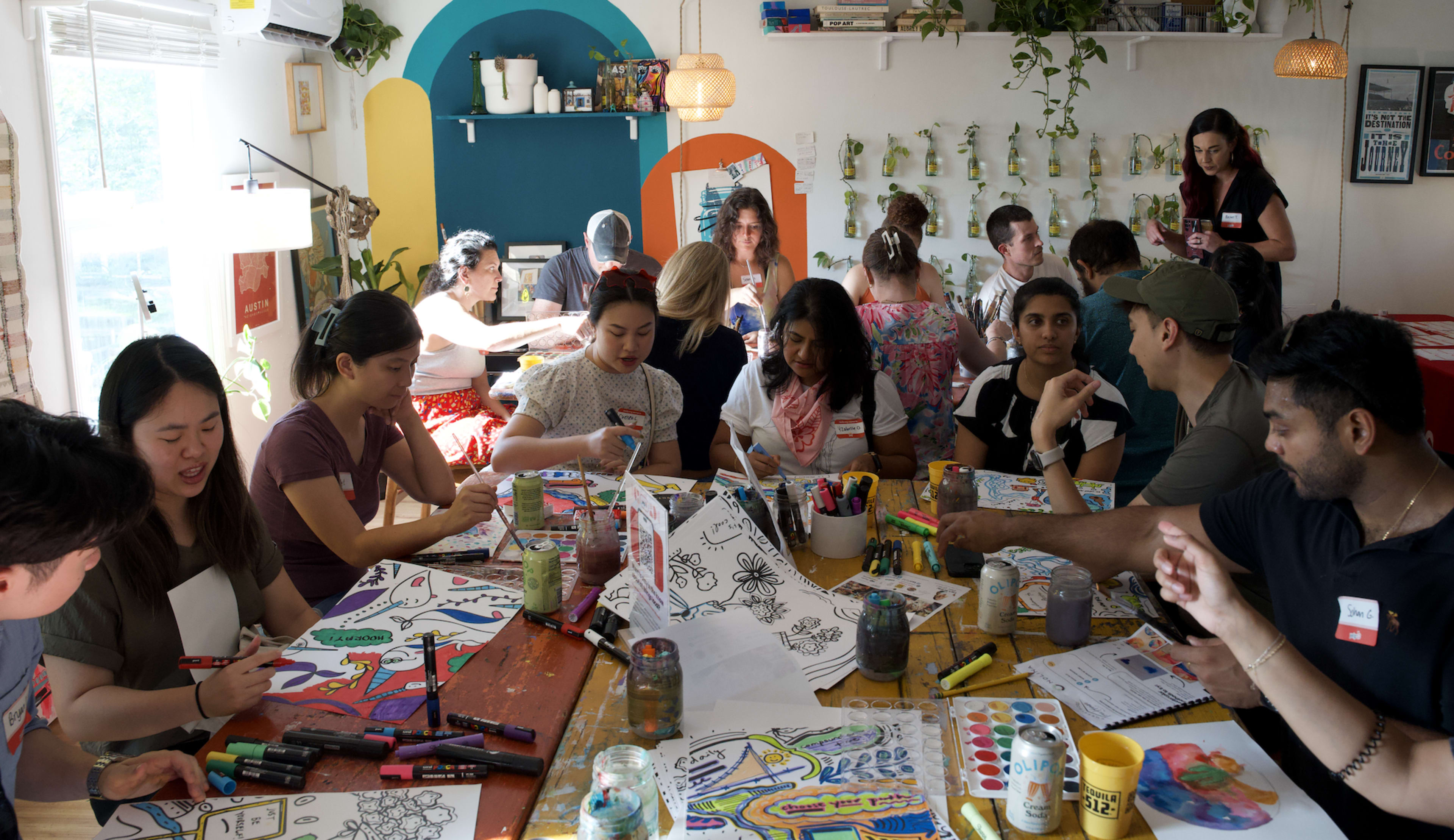 A group of people is engaged in a coloring activity at a communal table filled with art supplies and colorful drawings.