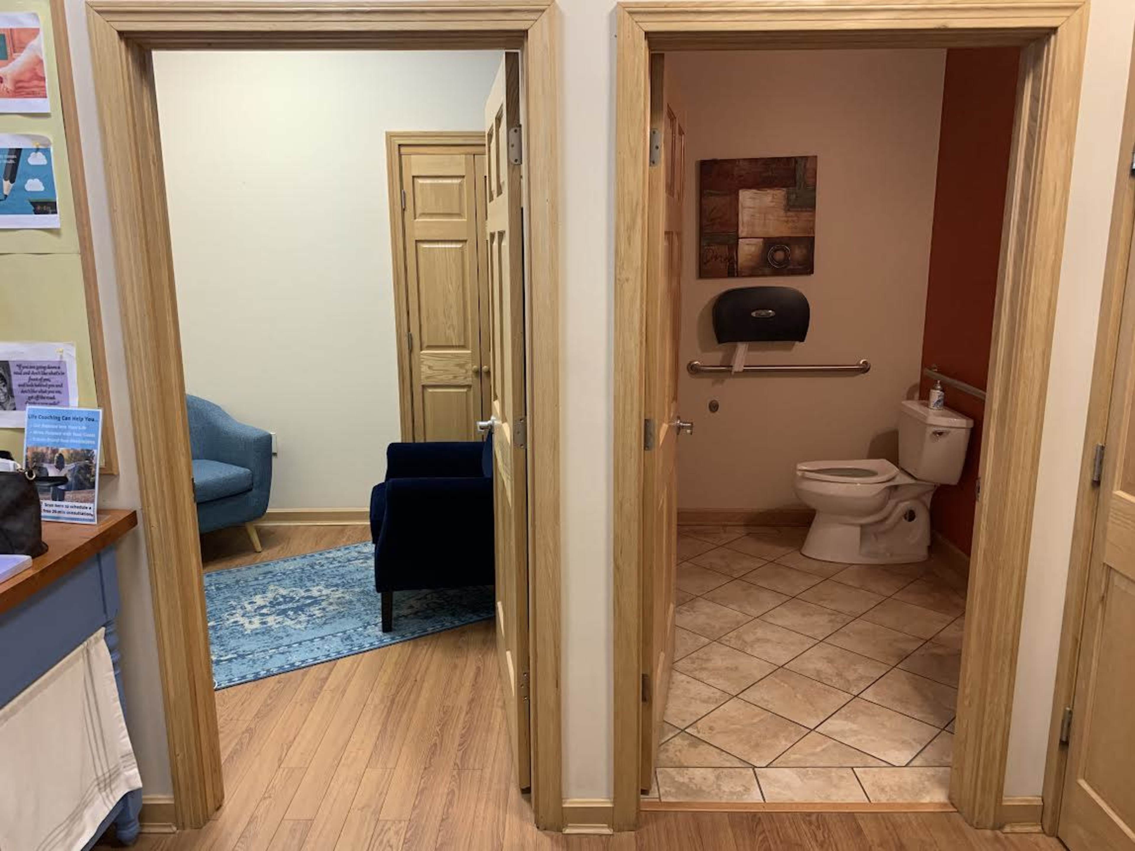 The image shows a hallway with two doorways, one leading to a small sitting area with a blue chair and the other leading to a bathroom with a toilet and sink.