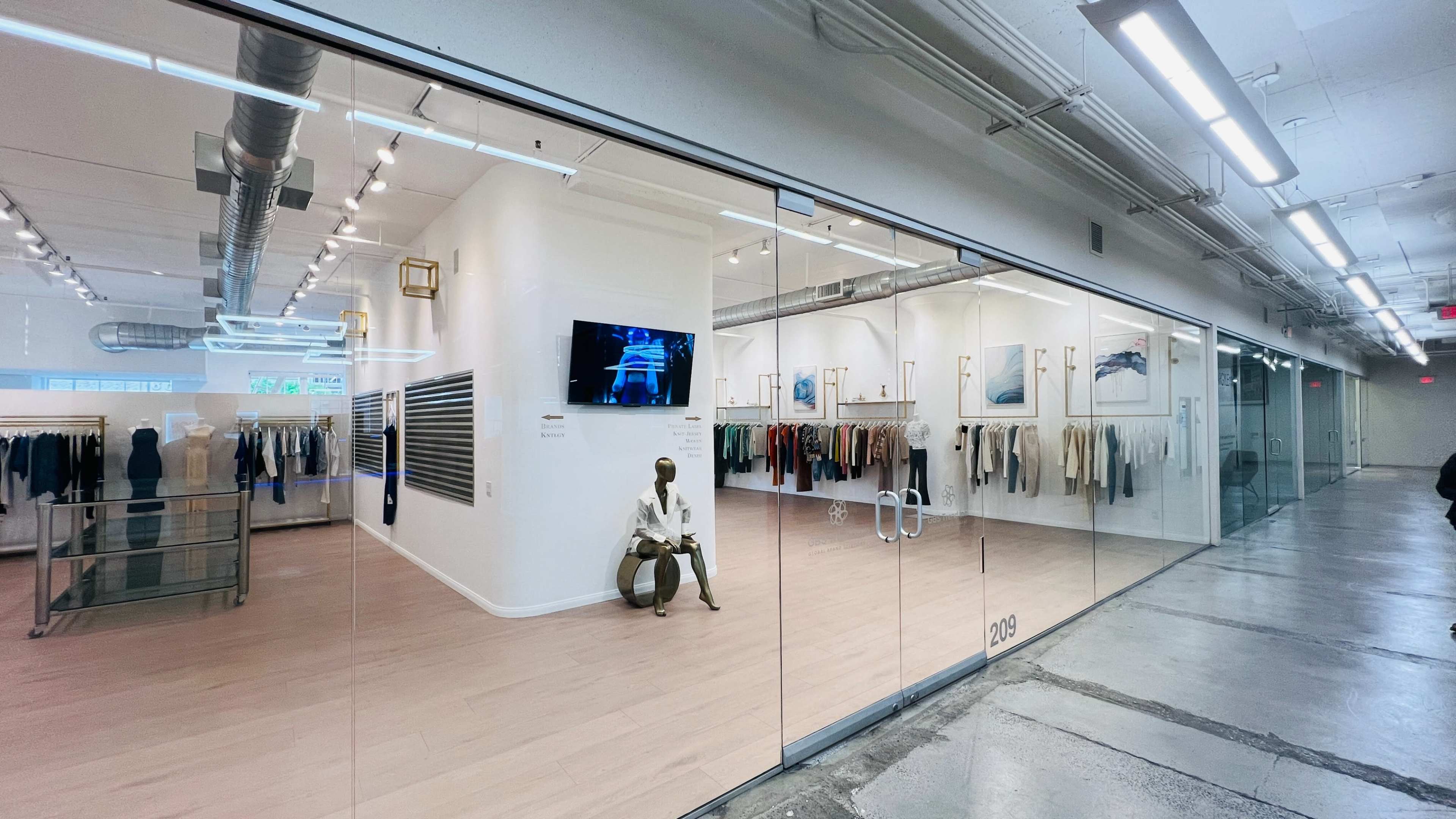 The image shows a modern retail space with glass walls displaying clothing racks and artwork inside.