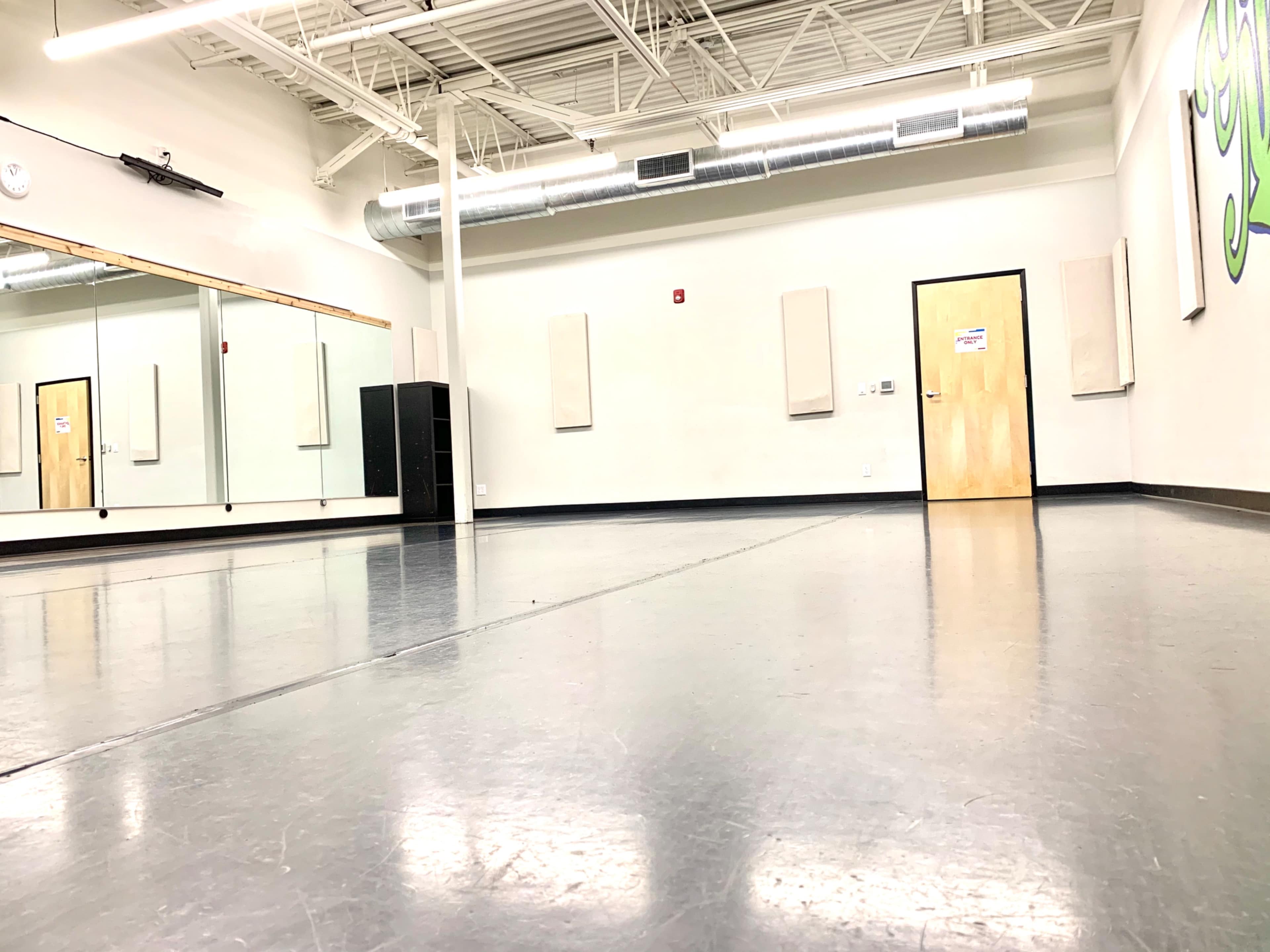 A spacious dance studio with a mirrored wall, wooden flooring, and muted decor.