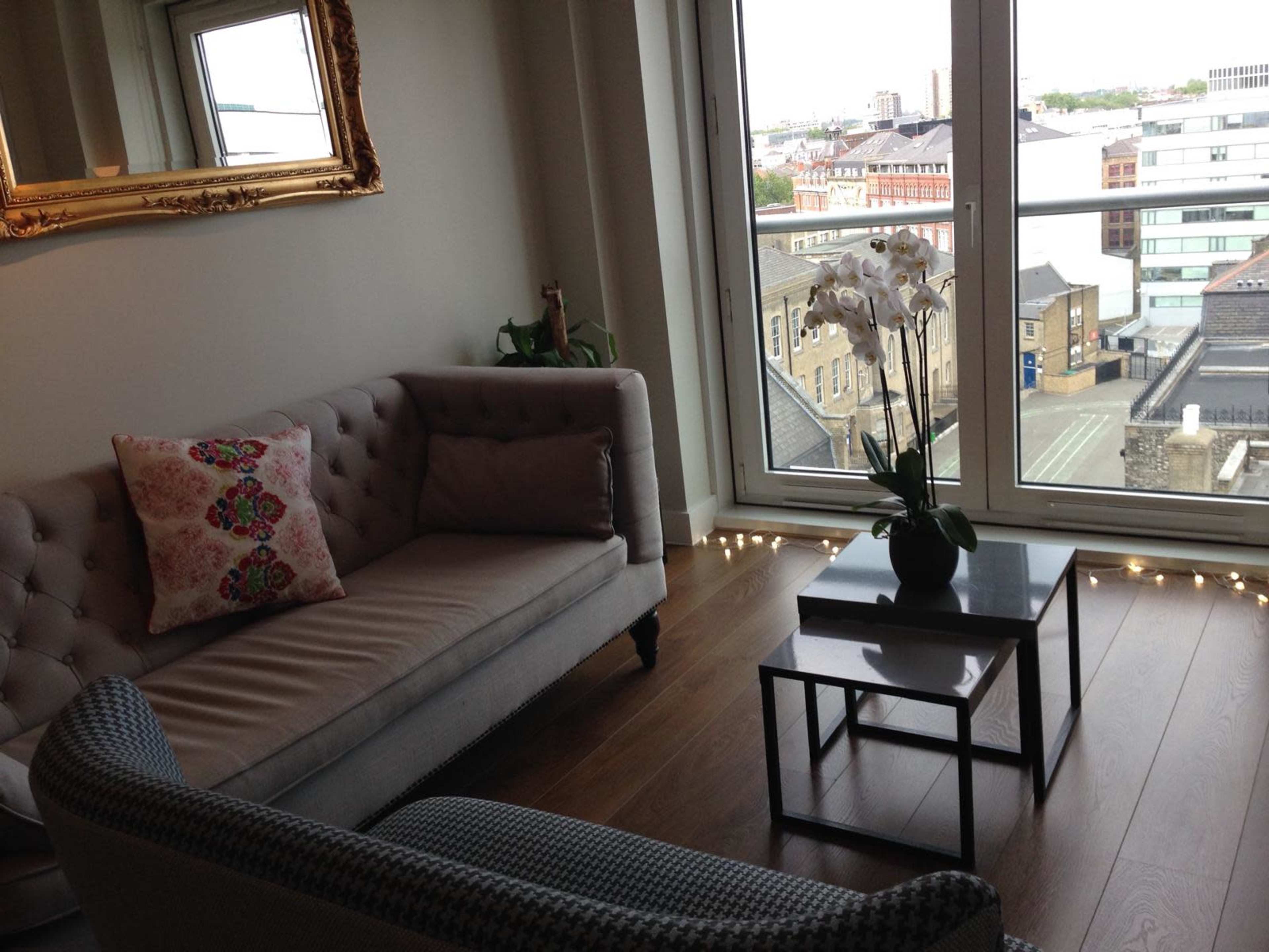 A cozy living room features a stylish sofa with decorative pillows, a small coffee table, and a view of the city through large windows.