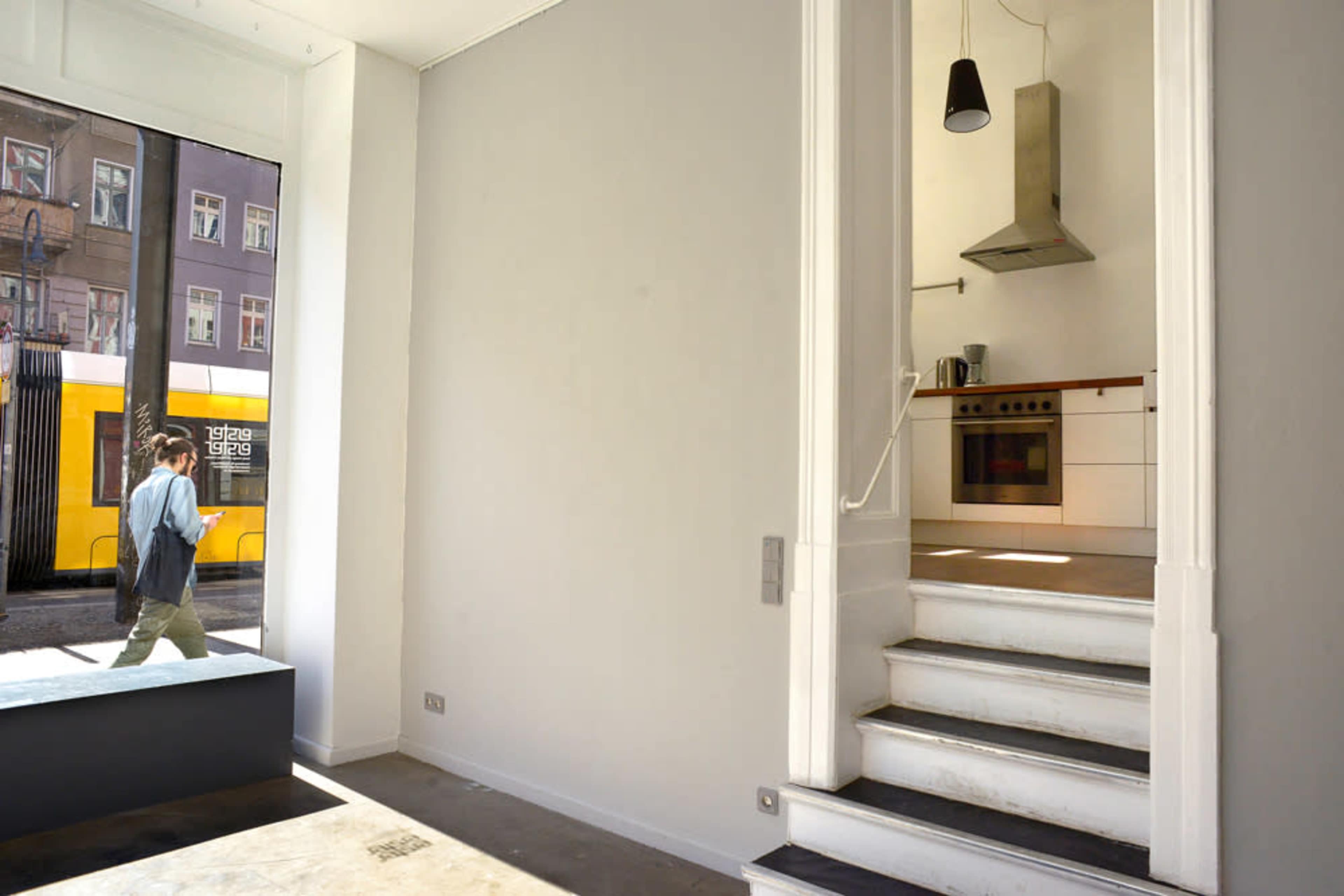 A person walks by a large window in a minimalist interior featuring an open staircase and a kitchen area.