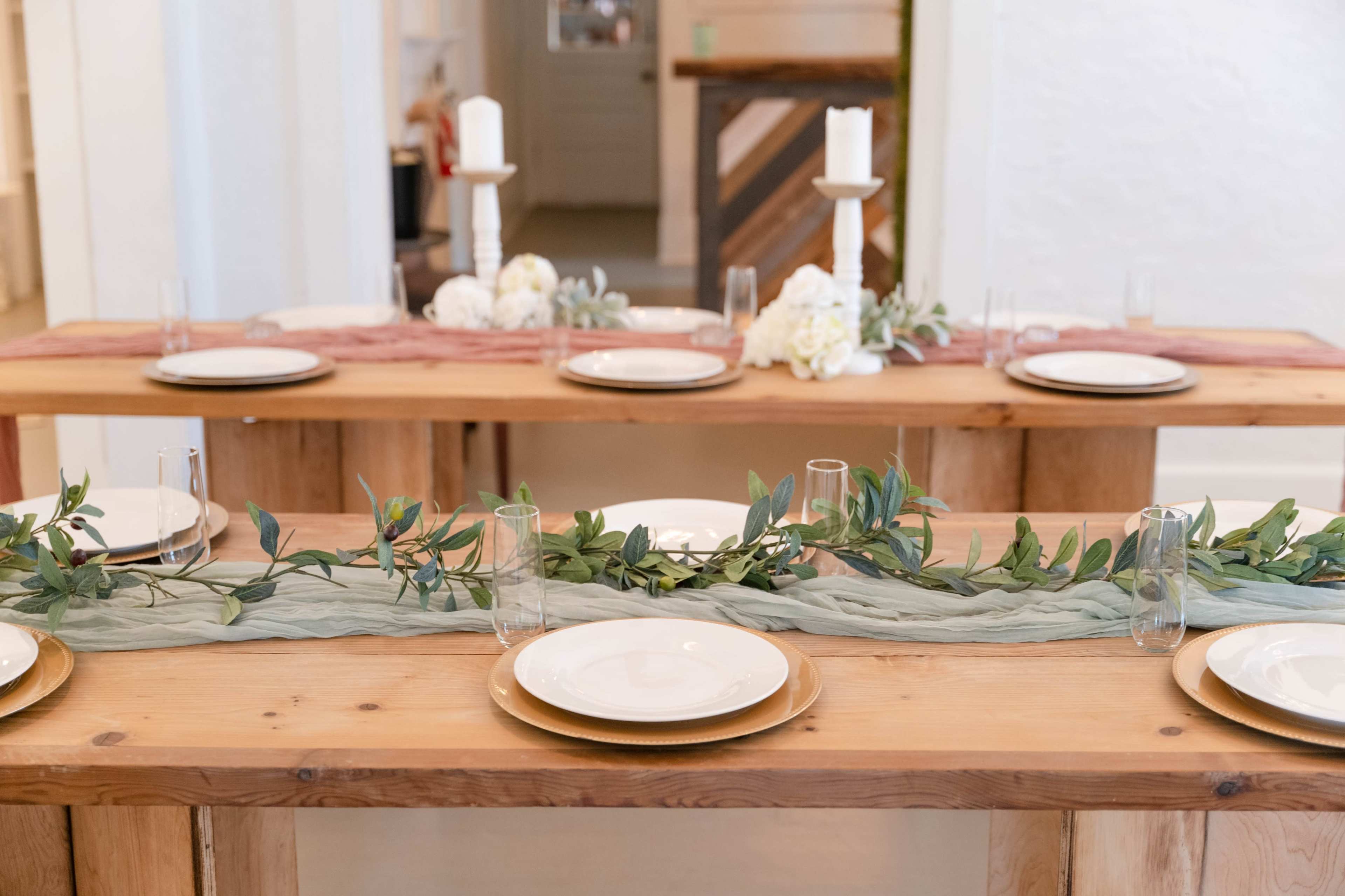 Two wooden tables set with plates, glasses, and decorative greenery.