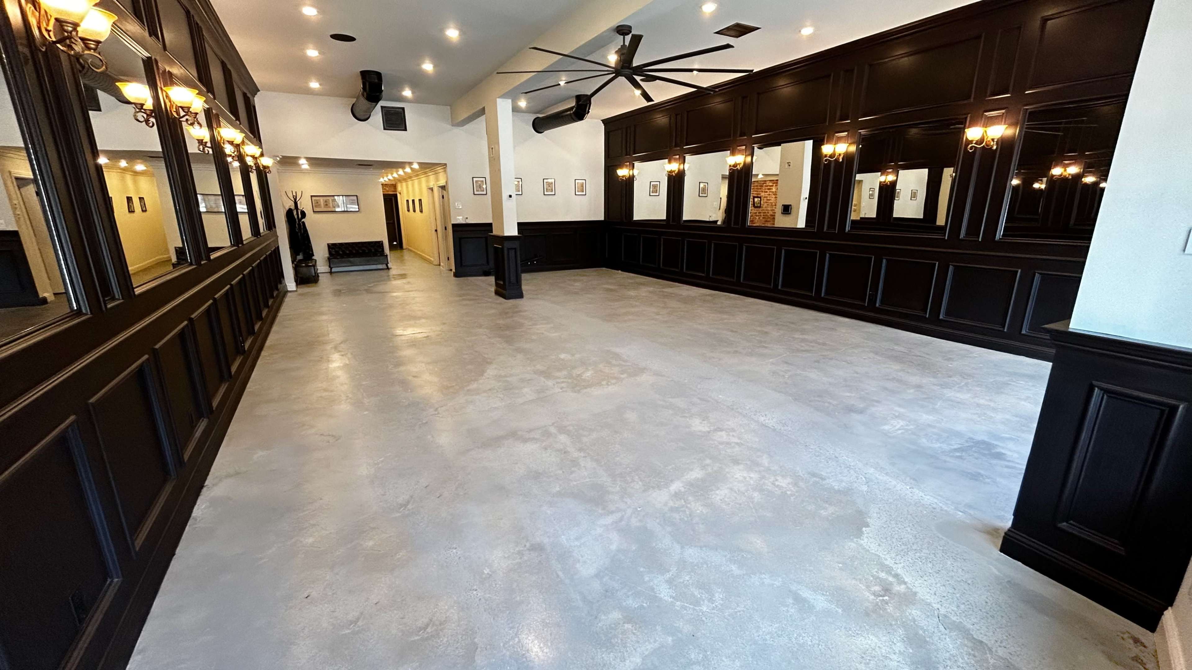 A spacious interior room with polished concrete flooring and dark wood paneling, featuring large mirrors and ceiling fans.