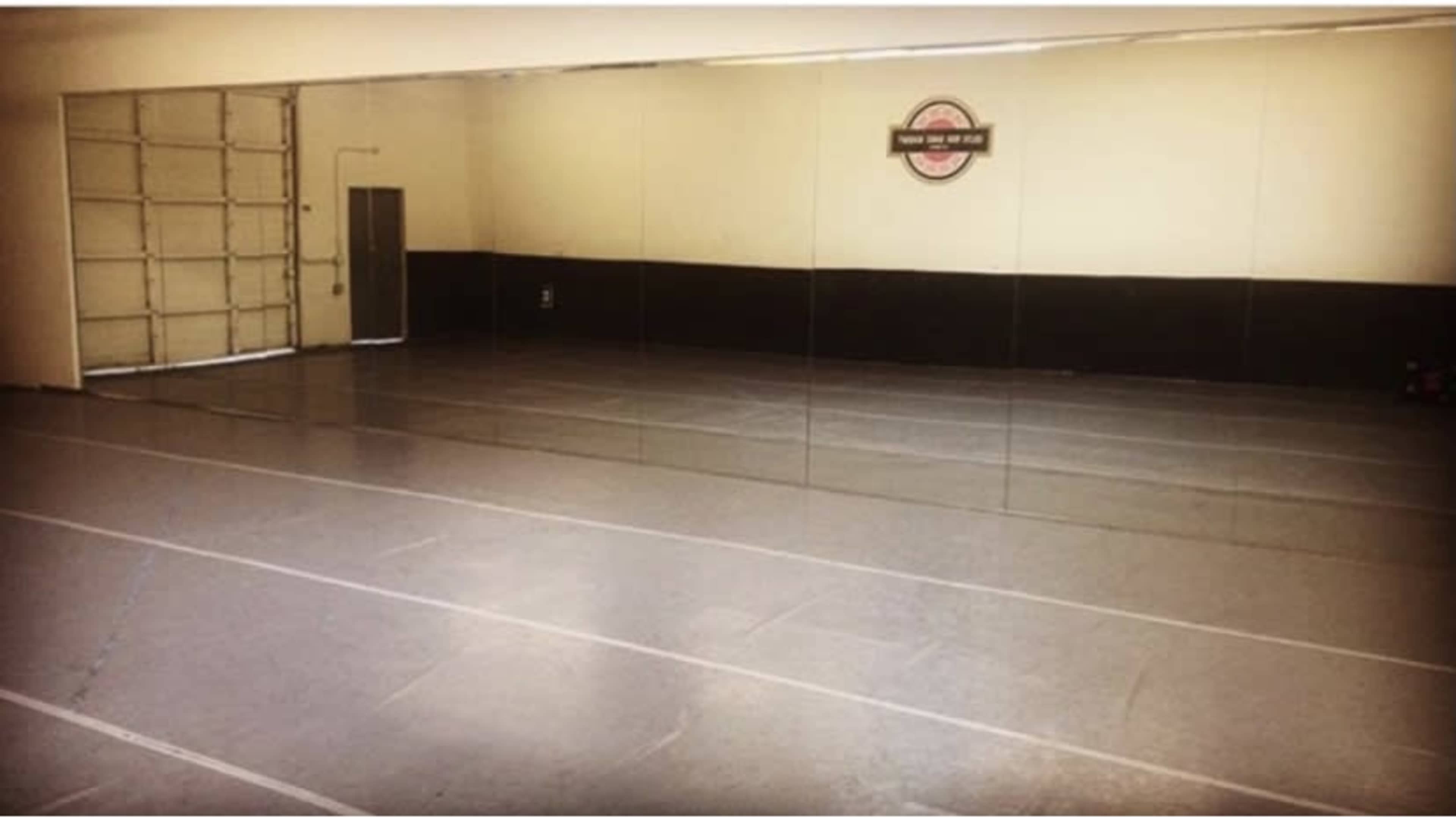 A spacious dance studio features mirrored walls and a smooth, reflective floor.