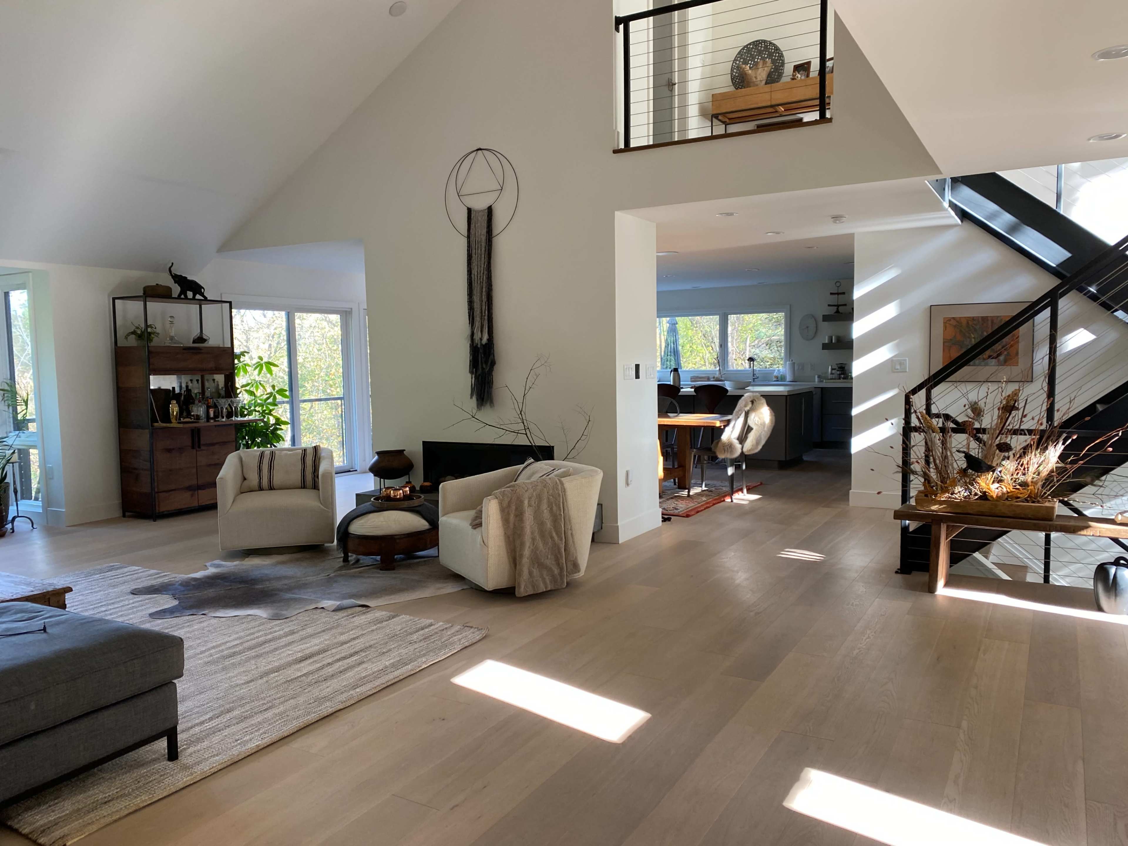 The interior of a modern home features an open layout with a living area, dining space, and kitchen visible, adorned with plants and natural light from large windows.