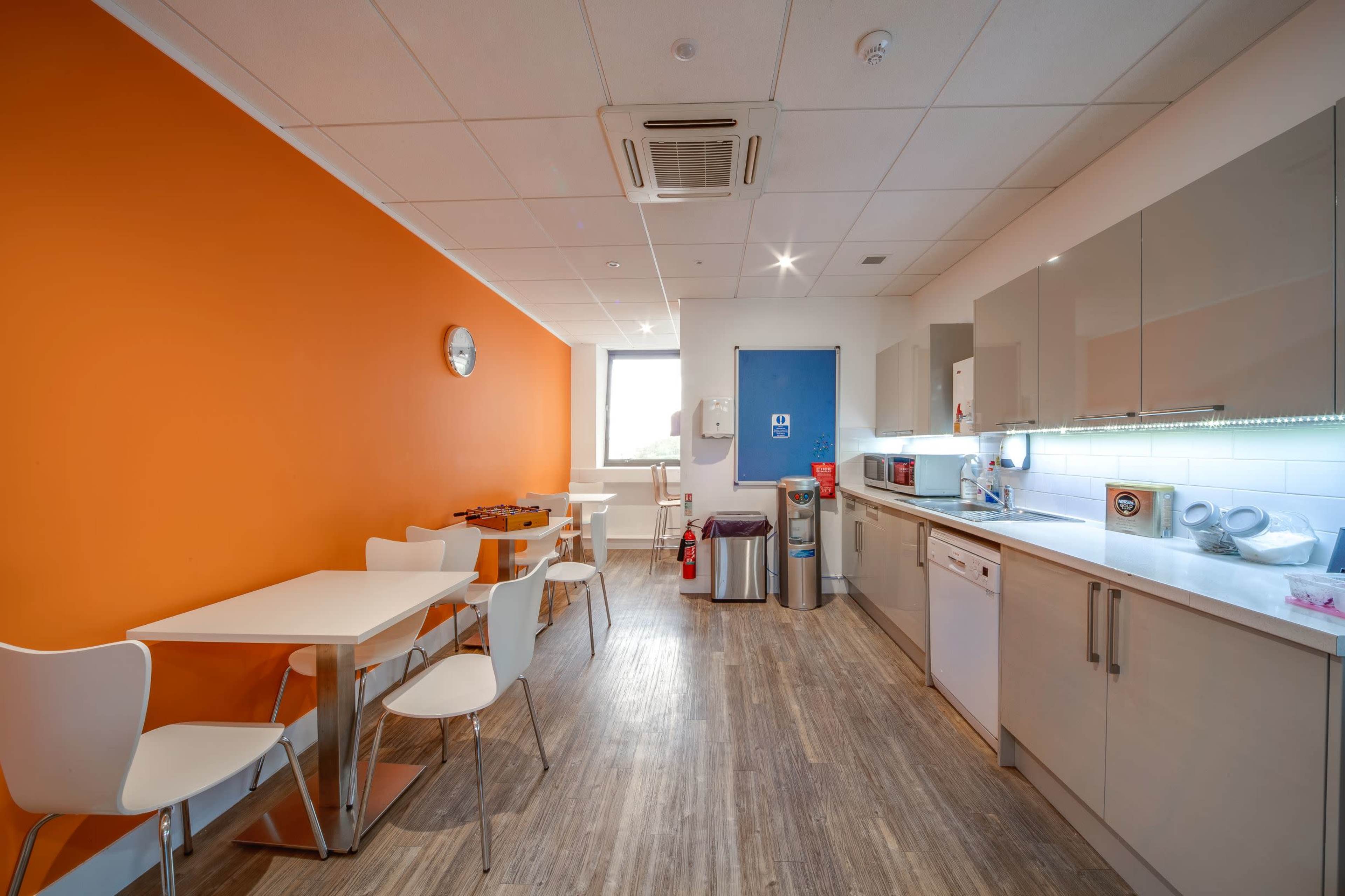 A kitchen area features an orange accent wall, a dining table with chairs, and appliances including a microwave, dishwasher, and refrigerator.