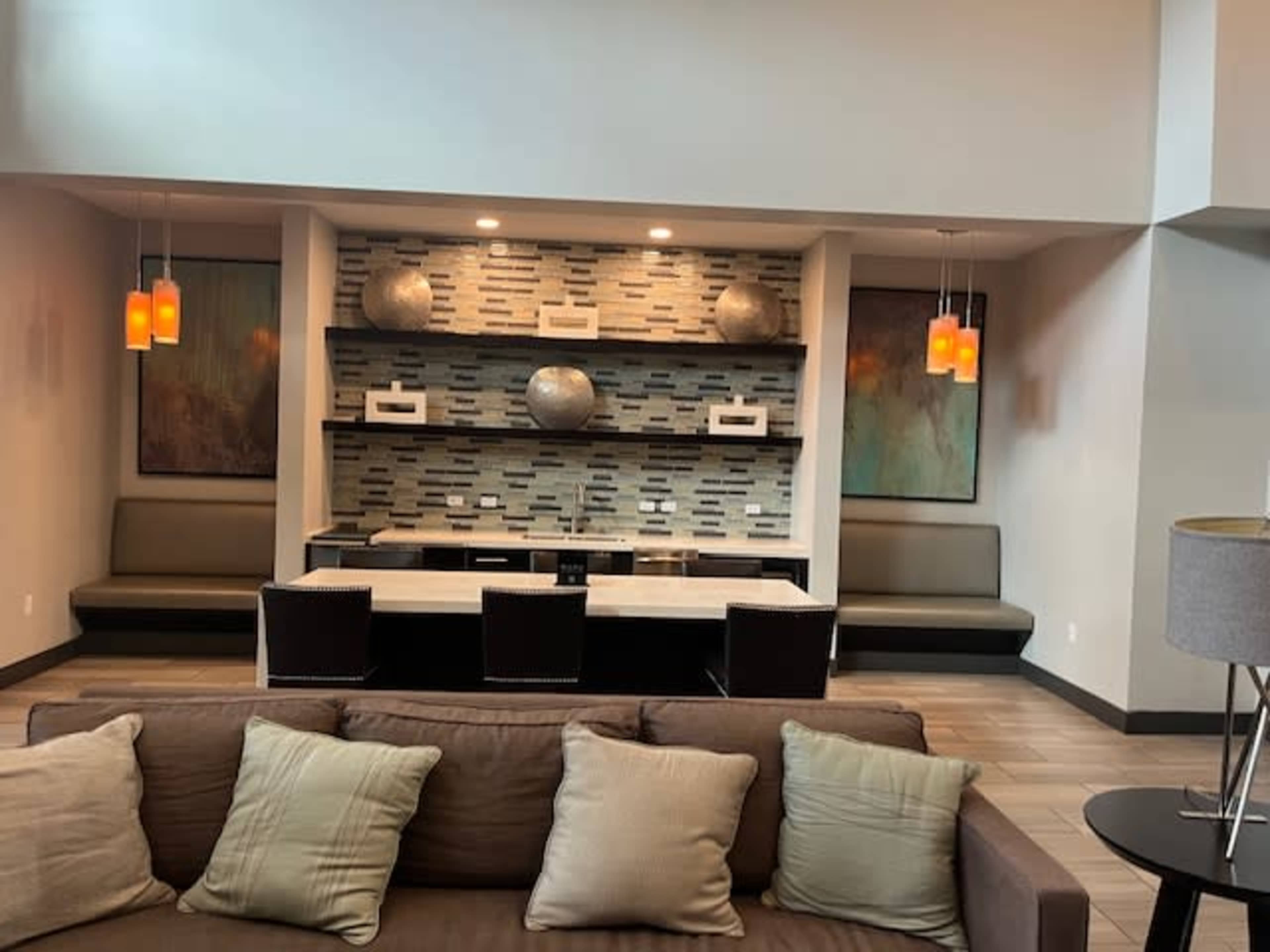 The image shows a modern lobby area featuring a sofa, a contemporary seating arrangement, and a decorative wall with shelves and lighting.