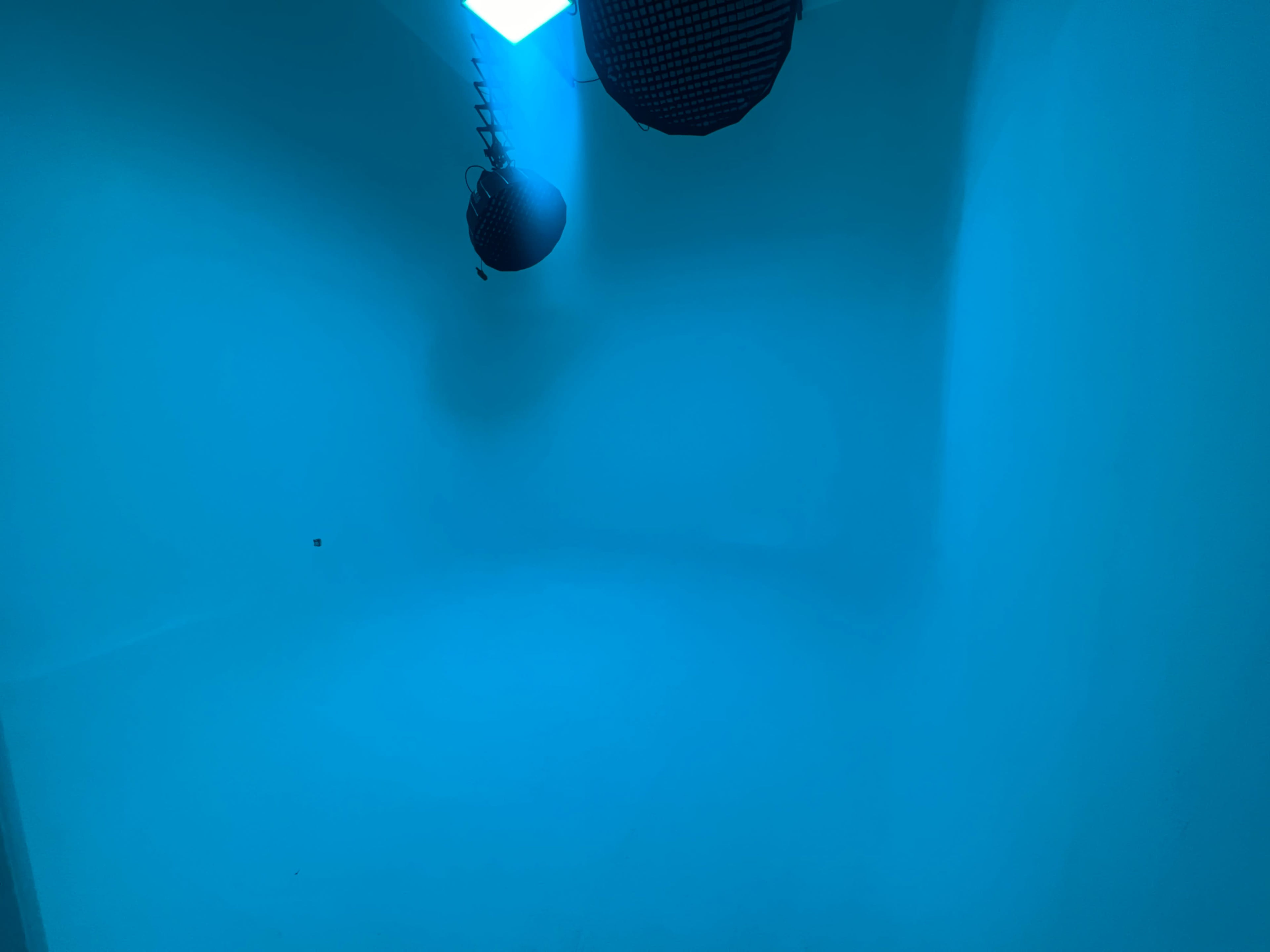 A room with blue walls and two hanging fixtures emitting blue light.