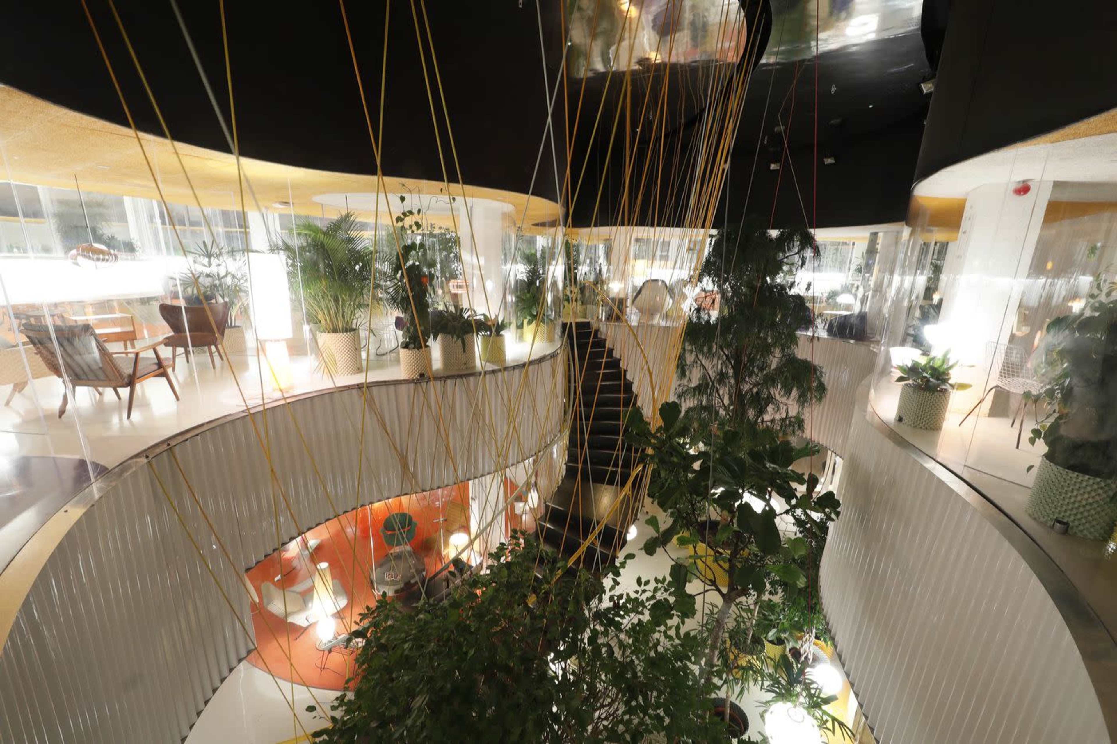 A modern interior of a multi-level restaurant featuring plants, elegant seating areas, and a curved staircase.