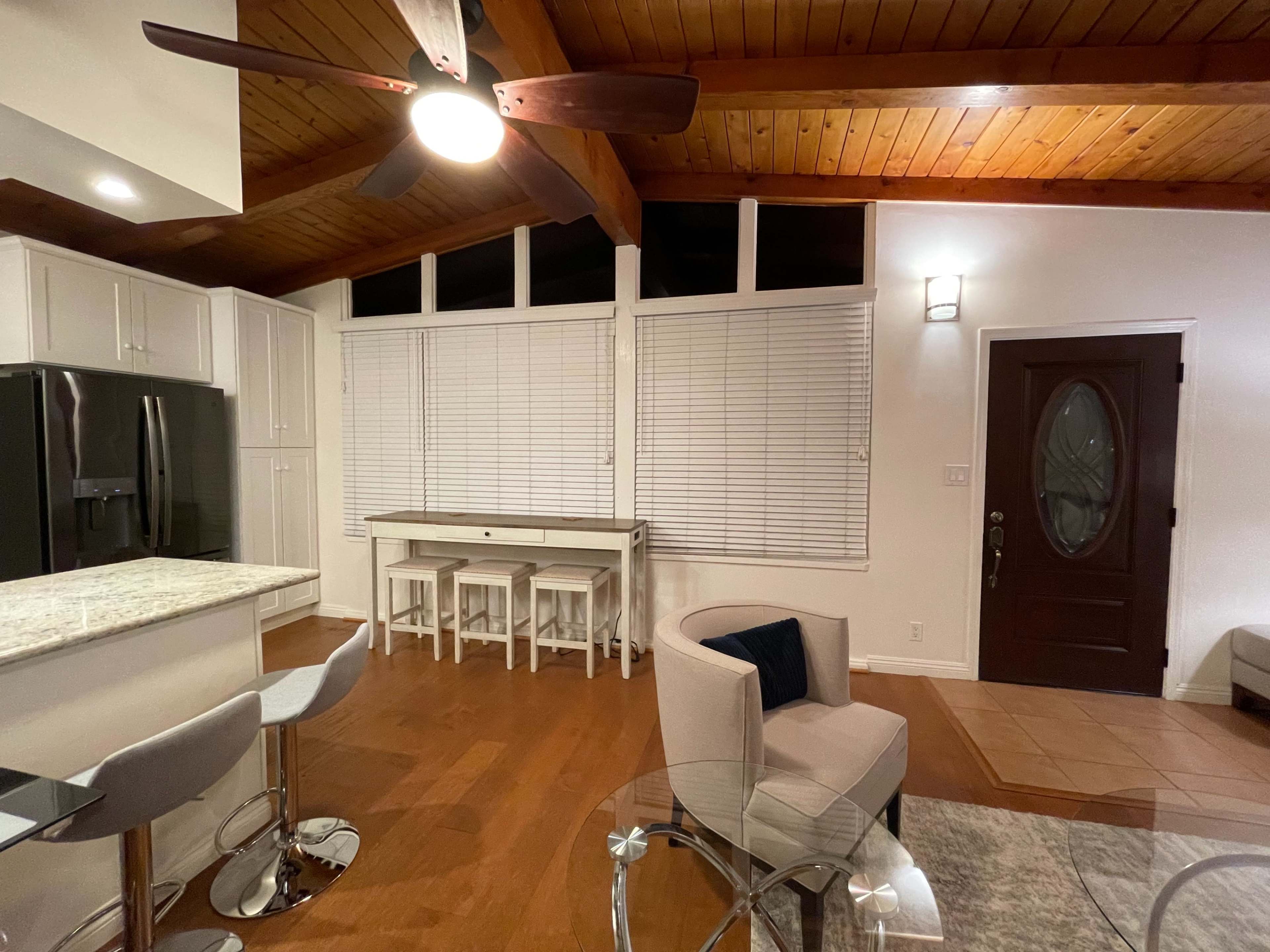 A modern living space with wooden beams, a kitchen island with seating, a dining table, and a front door with a window beside it.