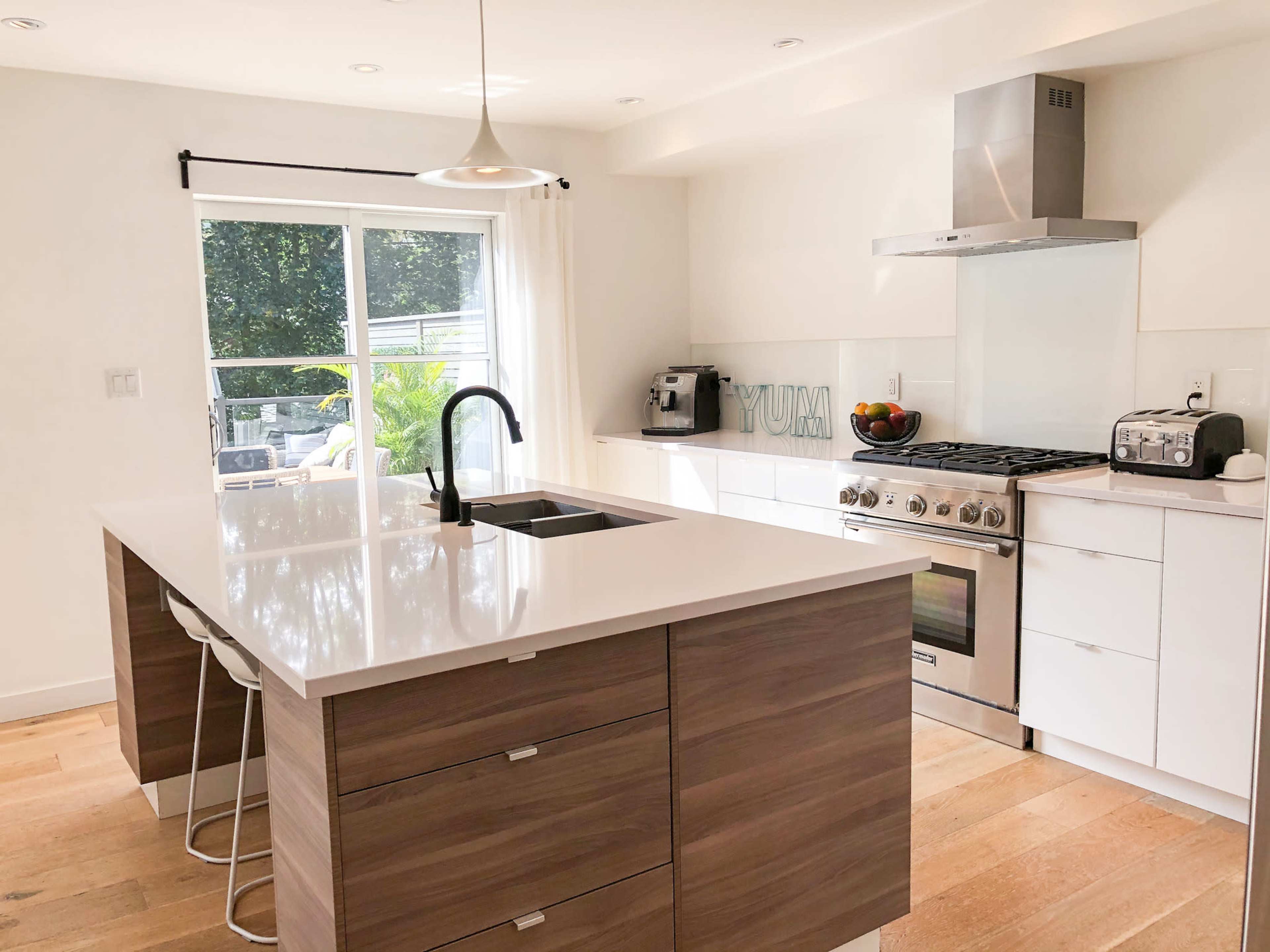 A modern kitchen with a central island, stainless steel appliances, and large windows allowing natural light to flow in.