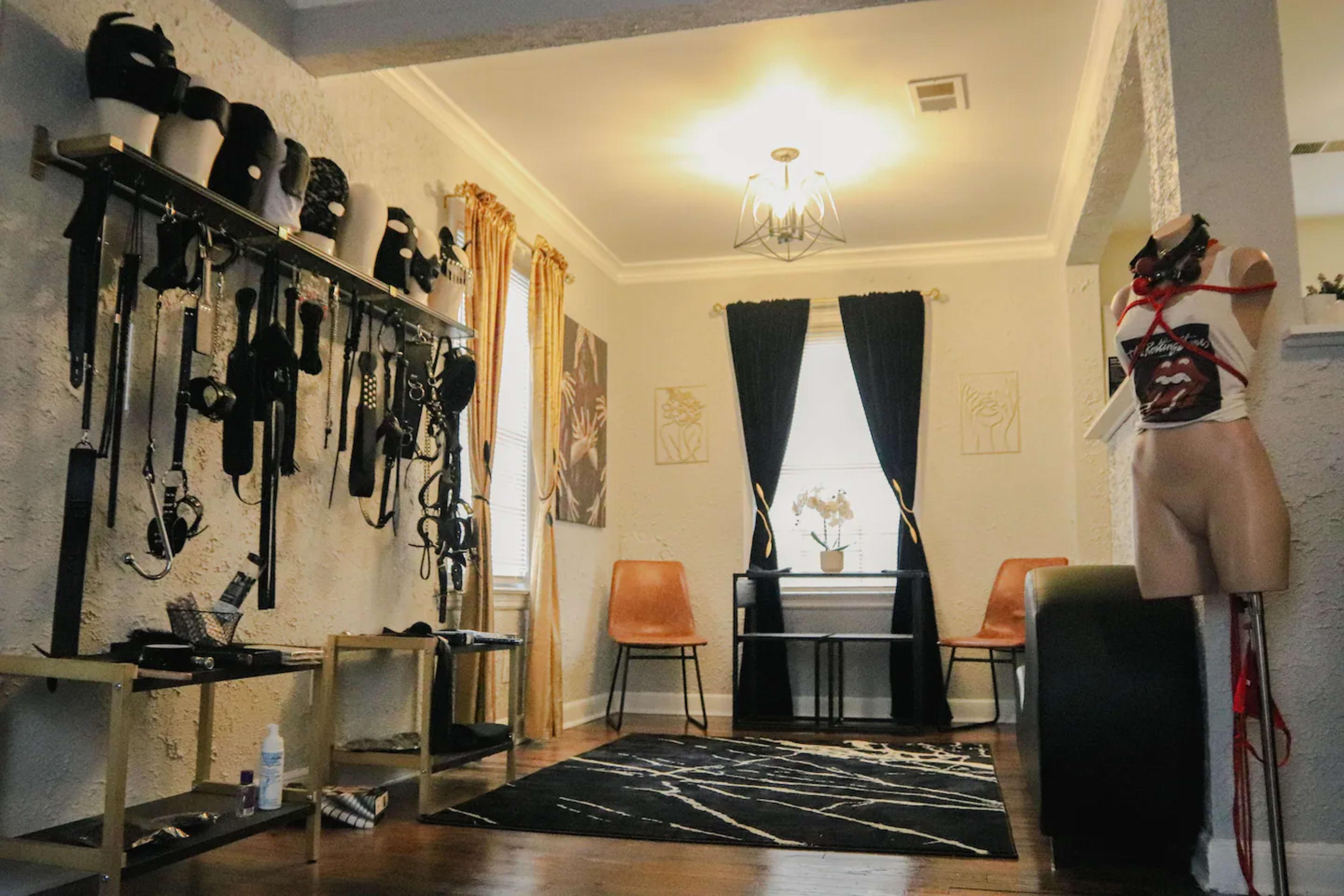 A room with a collection of harnesses and accessories displayed on racks, two chairs, and a small table with a plant in the center.