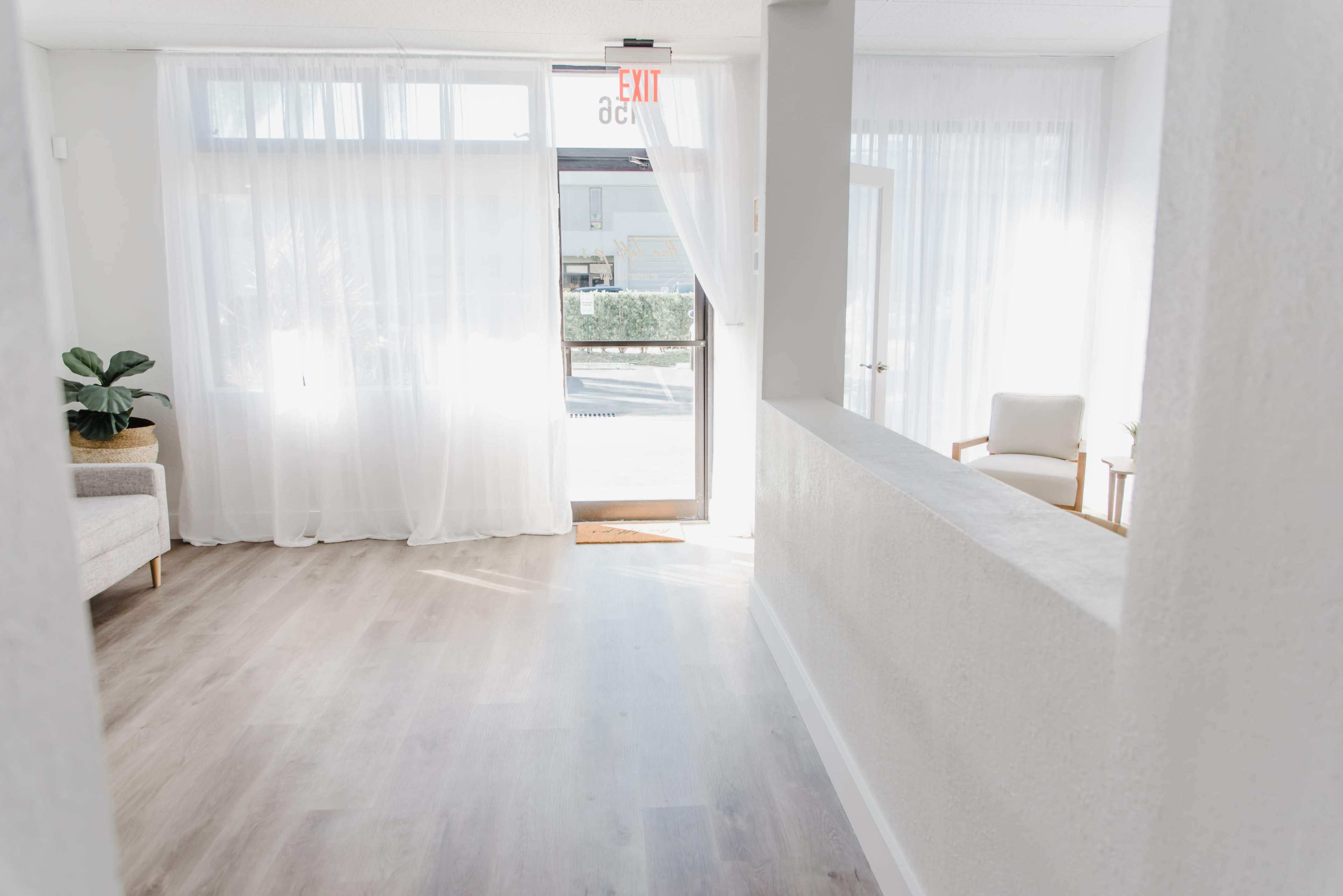 A bright, airy interior features a doorway with sheer curtains, leading to an exit, alongside a cozy seating area.