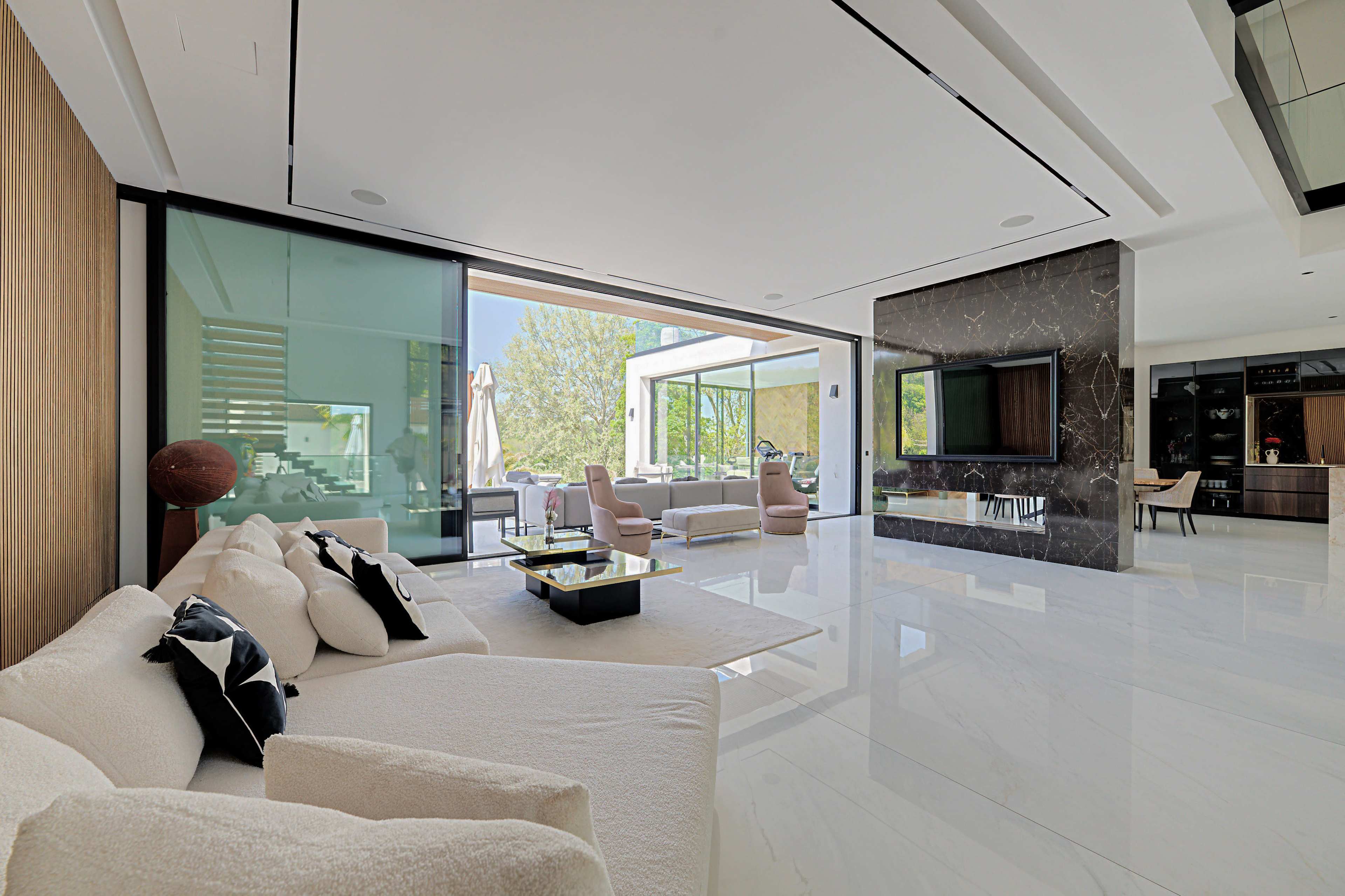 The image depicts a modern living room with large glass windows, minimalistic furniture, and an open layout featuring a marble accent wall.