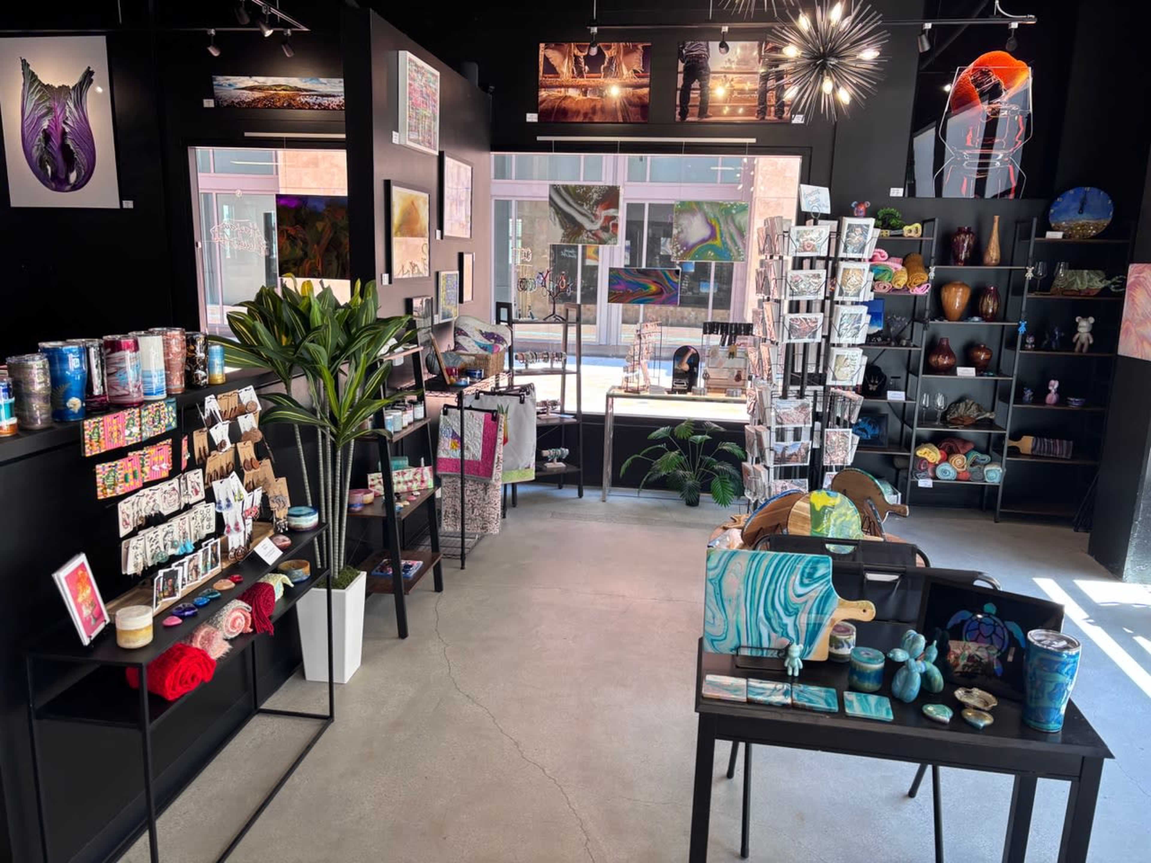 The image depicts the interior of a modern retail store filled with various art pieces, crafts, and decorative items, organized on shelves and display tables.