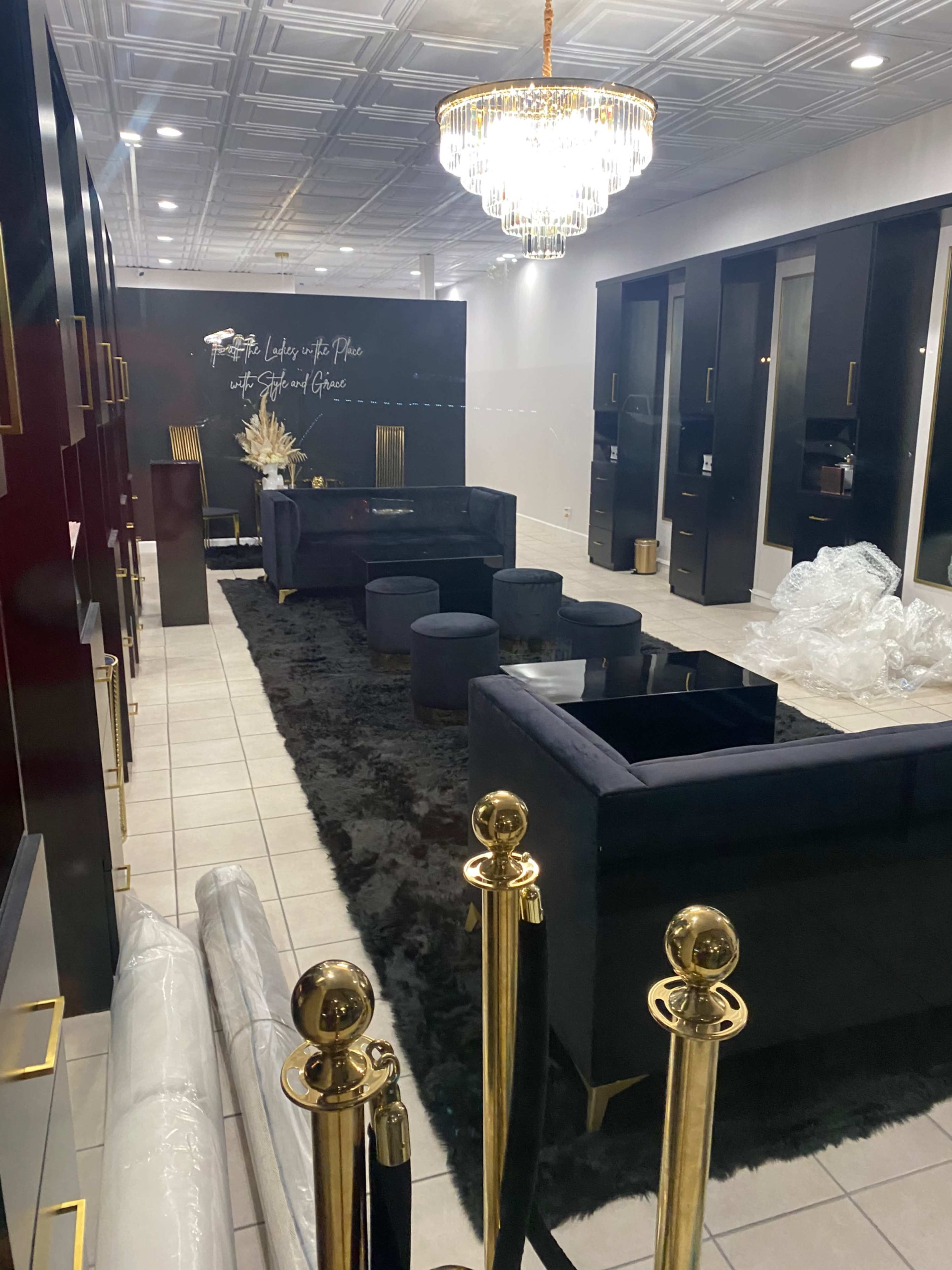 The image shows a modern lounge area with black furniture, a chandelier, and decorative elements against a backdrop of white walls and a tiled floor.