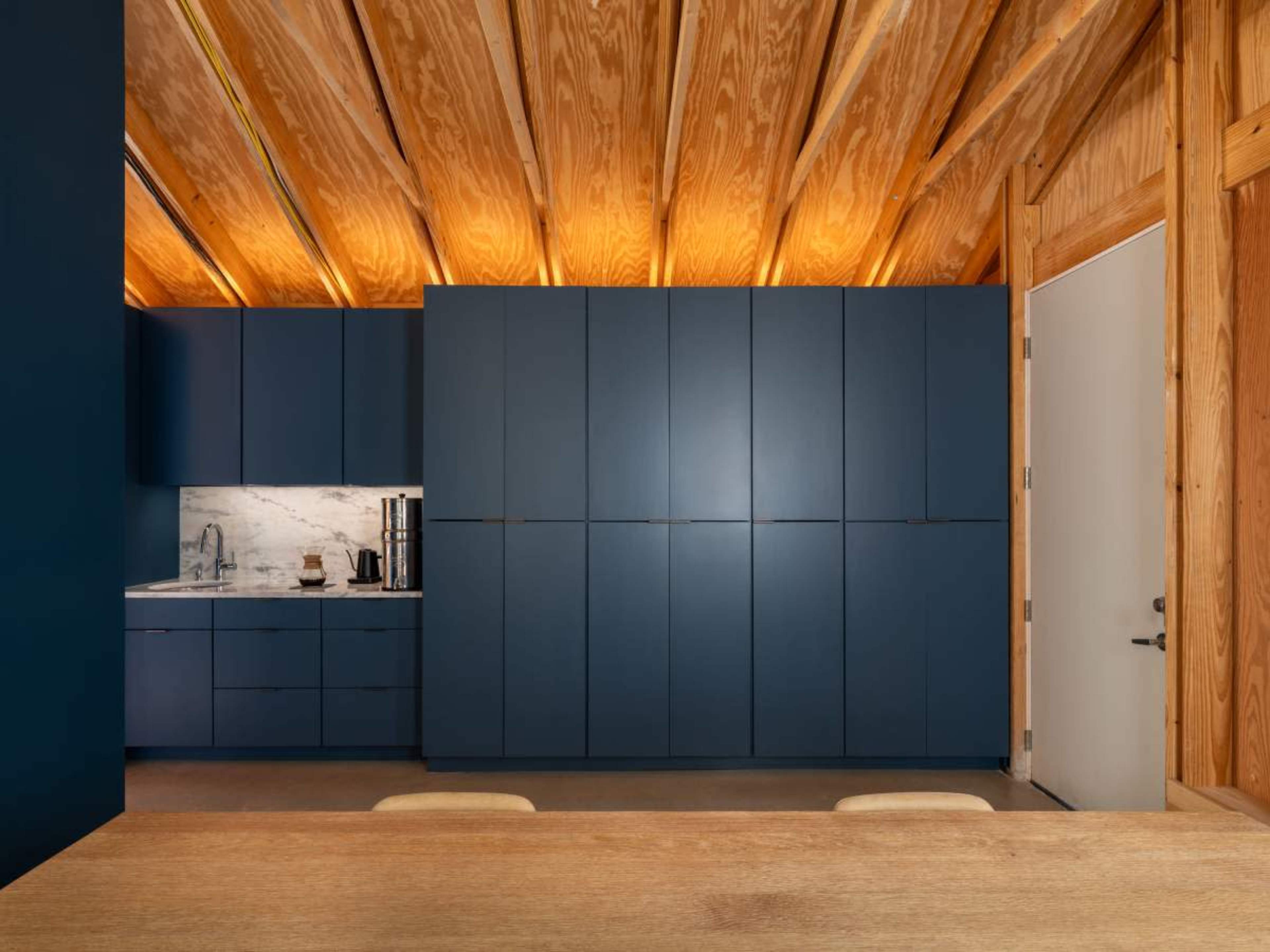 A modern kitchen features dark blue cabinetry, marble countertops, and a wooden beam ceiling.