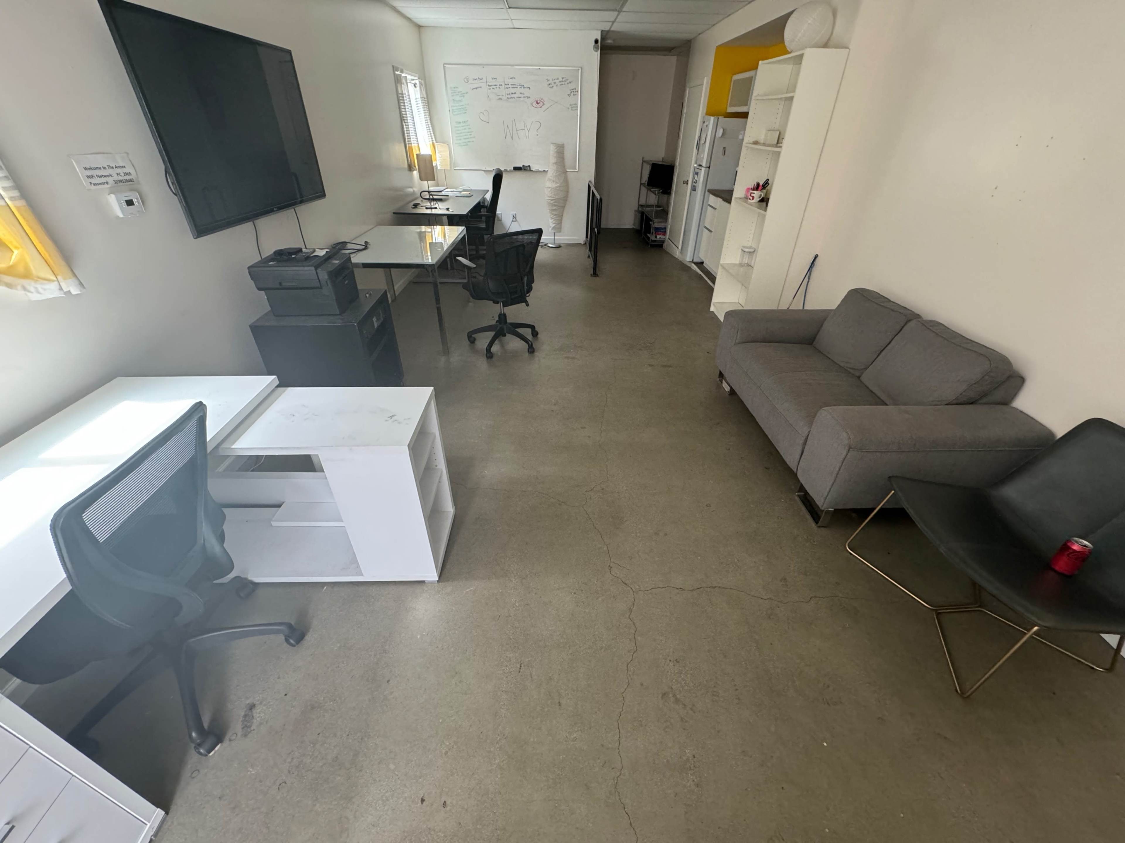 An office space with two desks, a couch, and a television mounted on the wall.