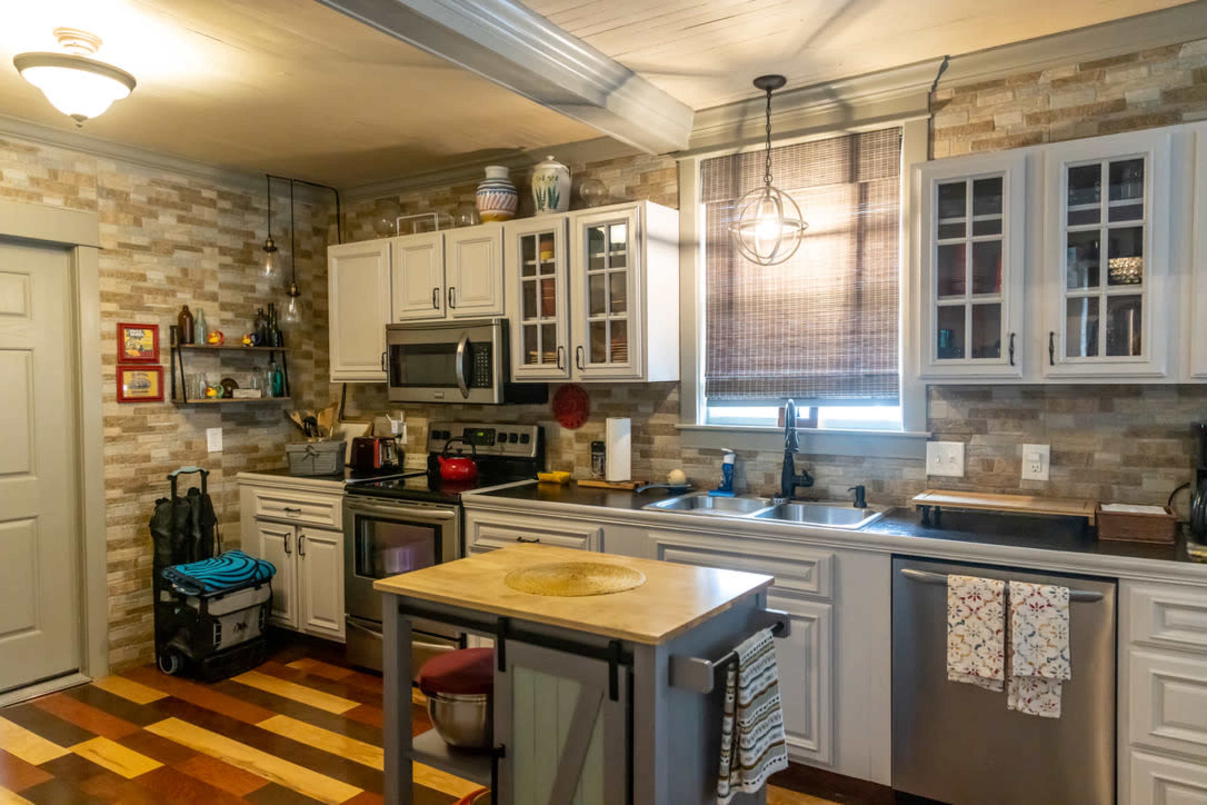 A modern kitchen with light-colored cabinets, a stainless steel sink, and a central island with a round top, set against a wall of textured stone.