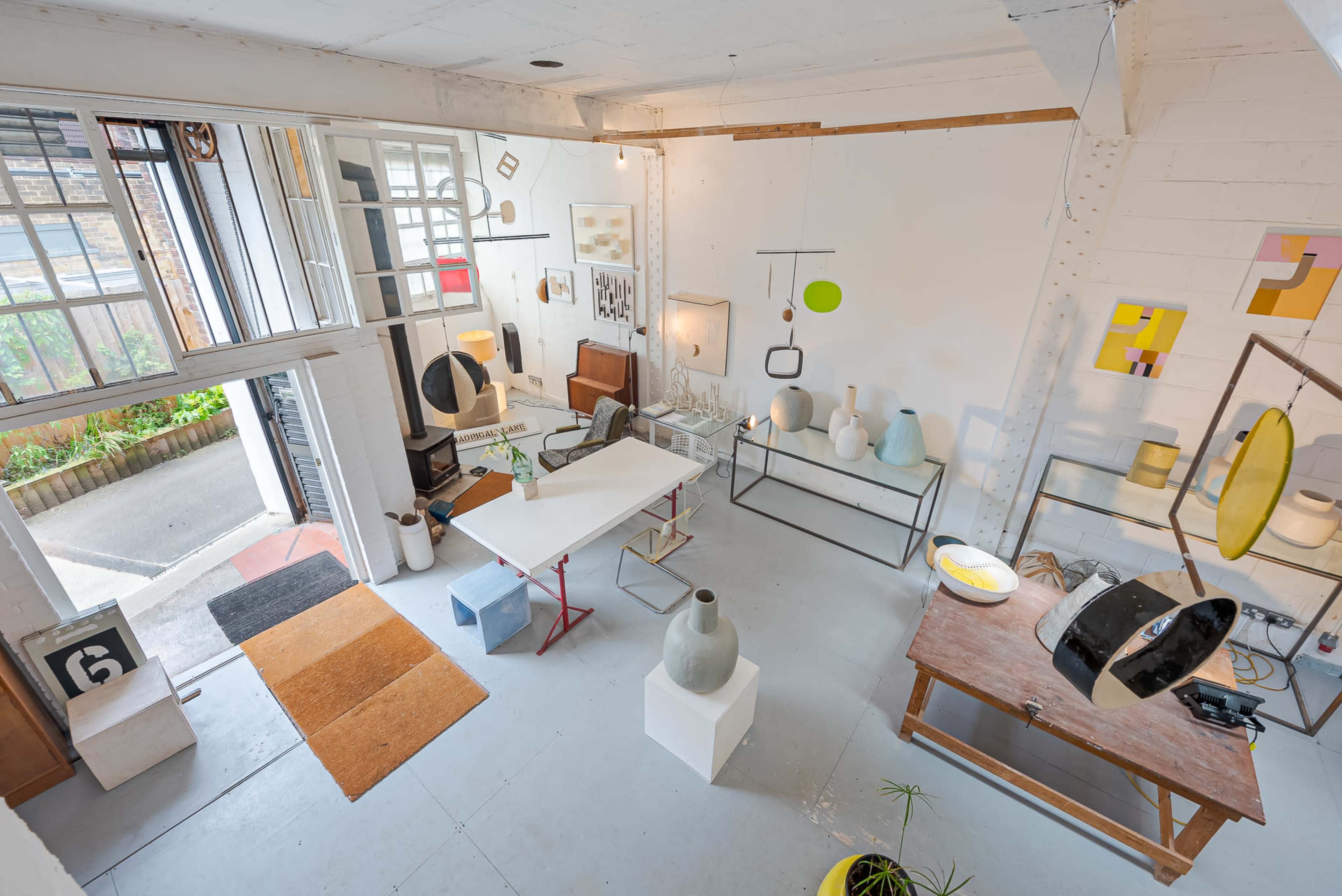 The image shows an art studio featuring various artworks and sculptures on display, with a large window allowing natural light to enter the space.