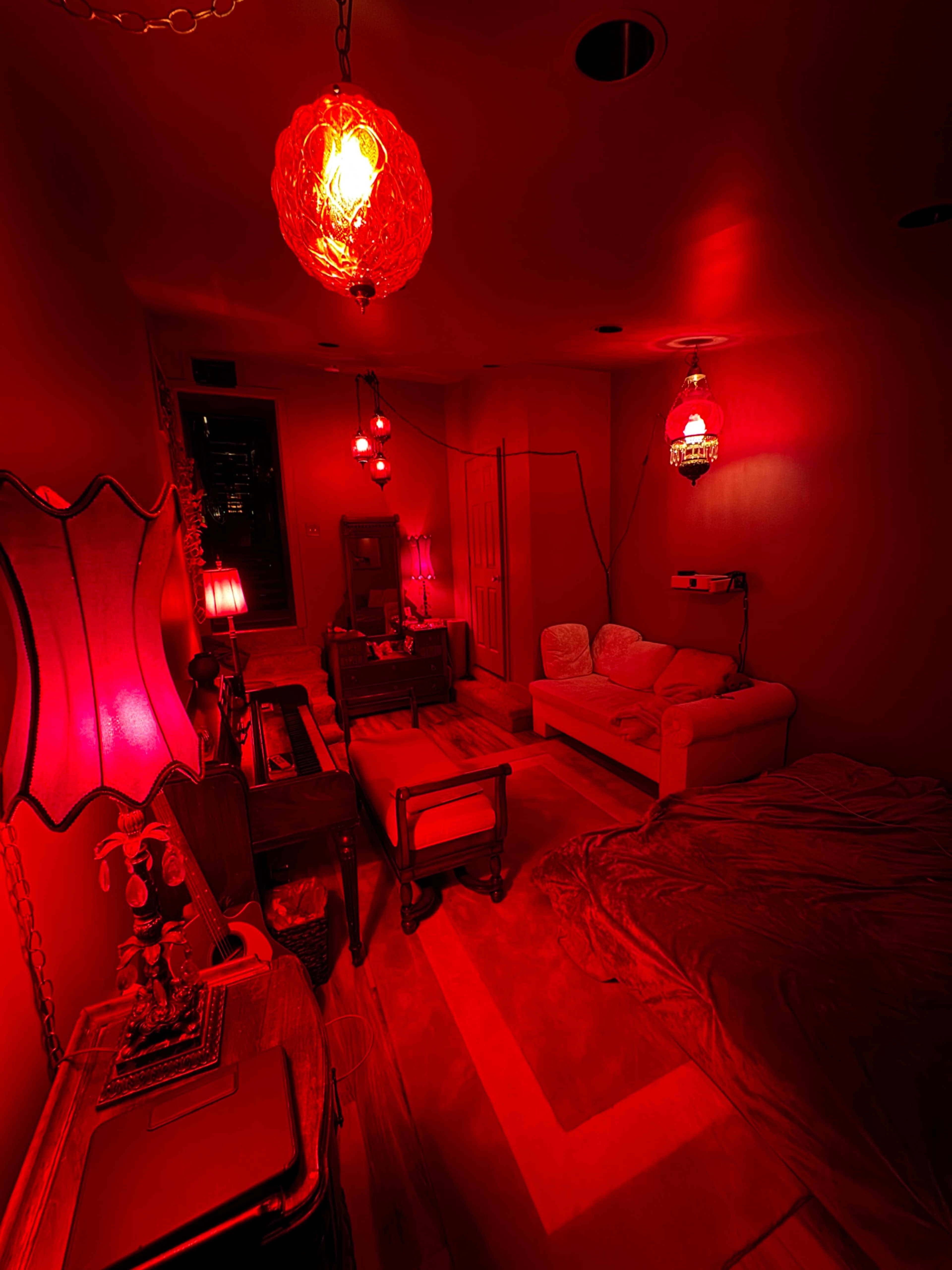 The room is dimly lit with red lights, featuring a couch, a piano, and various lamps along the walls.