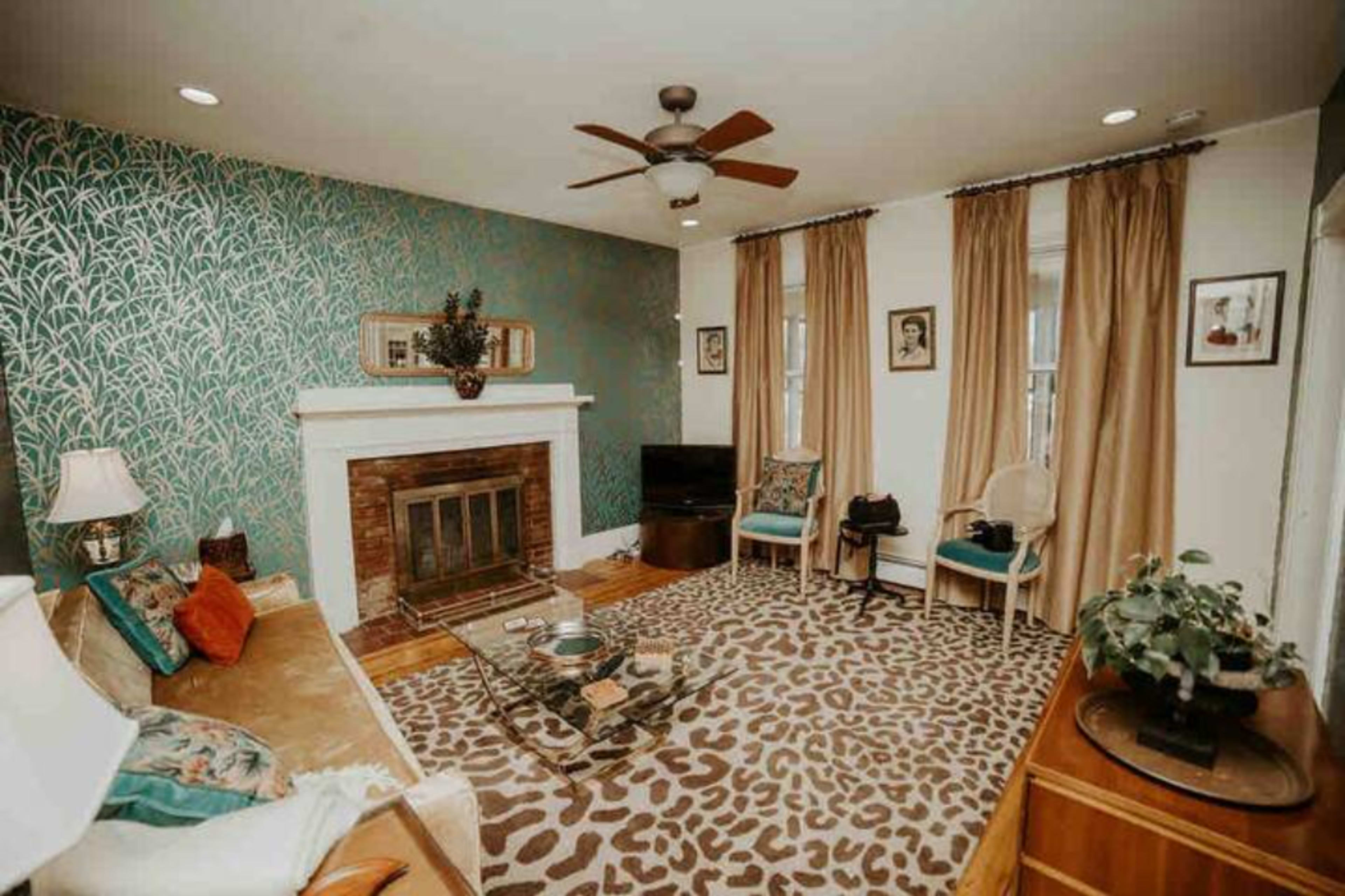 The living room features a fireplace, patterned rug, blue accent wall, and large windows with drapes.