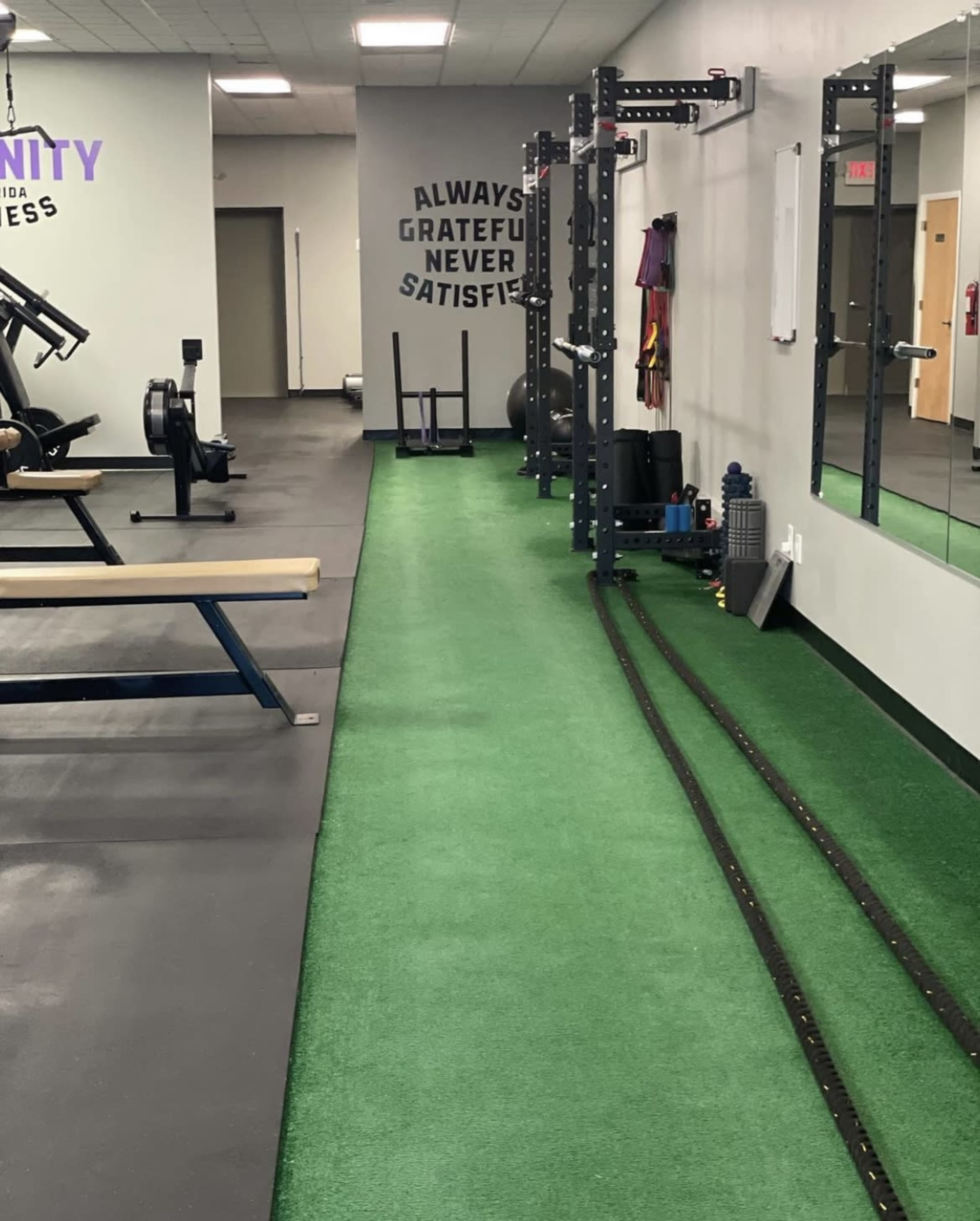 A fitness gym interior with artificial turf flooring, weightlifting equipment, and motivational quotes on the walls.