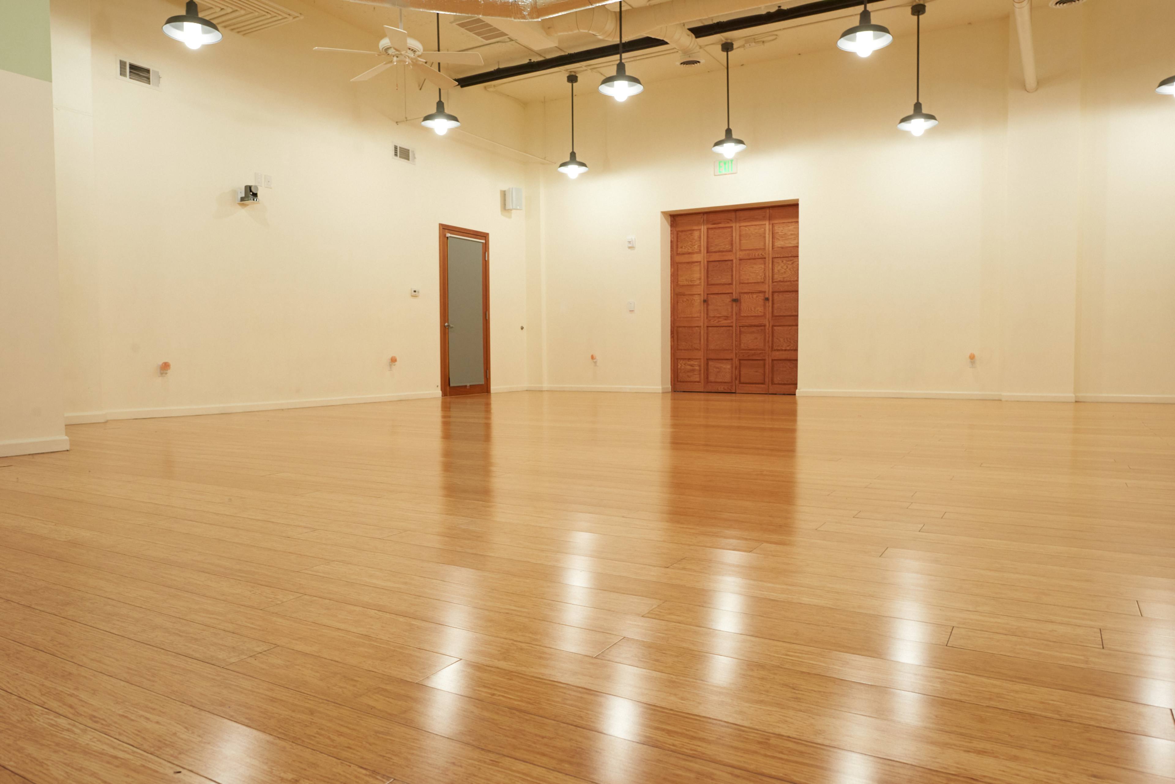 An empty room with wooden flooring, white walls, and a large wooden door at one end.