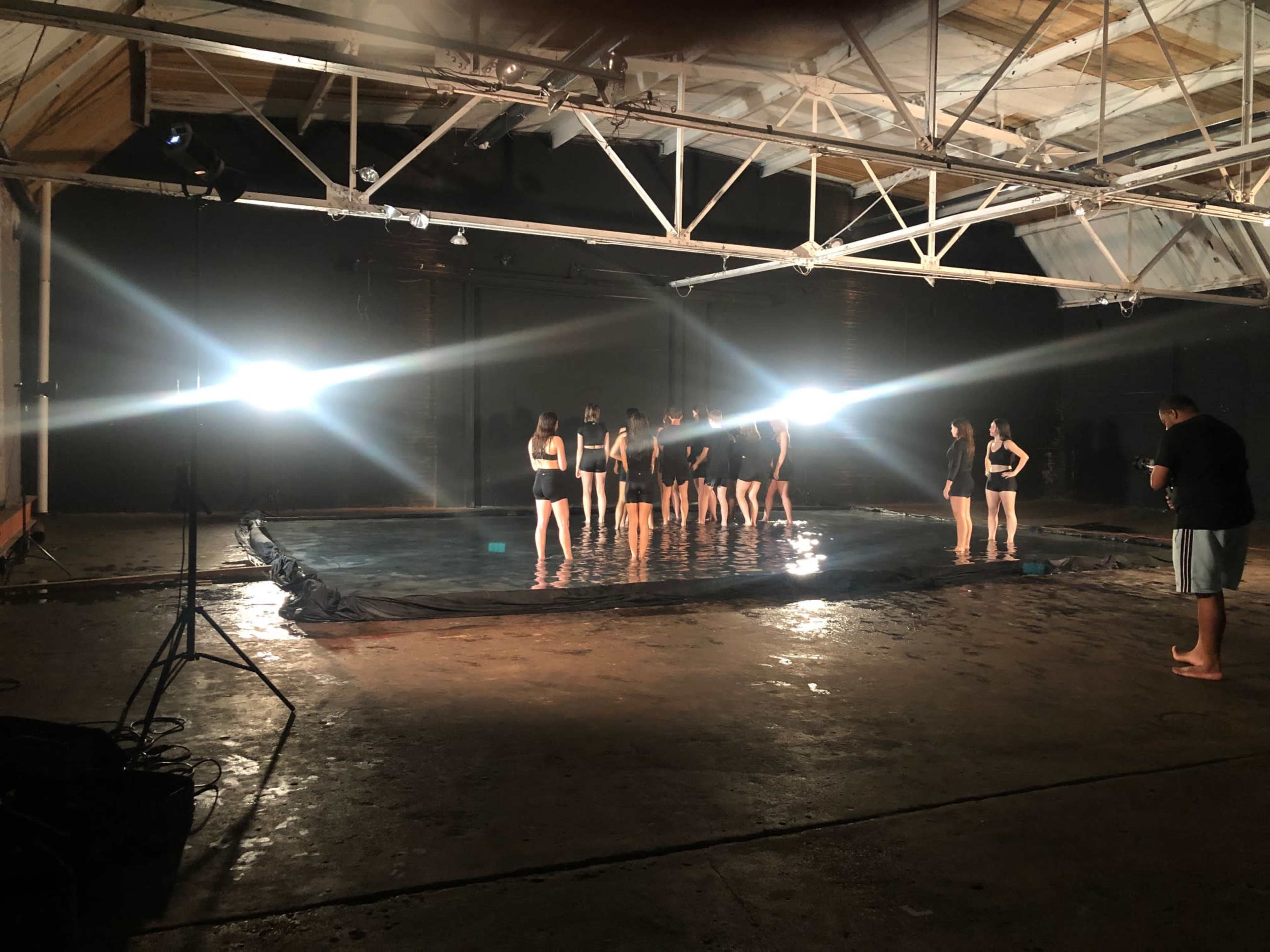 A group of individuals stands in a pool of water illuminated by bright lights in an industrial space.