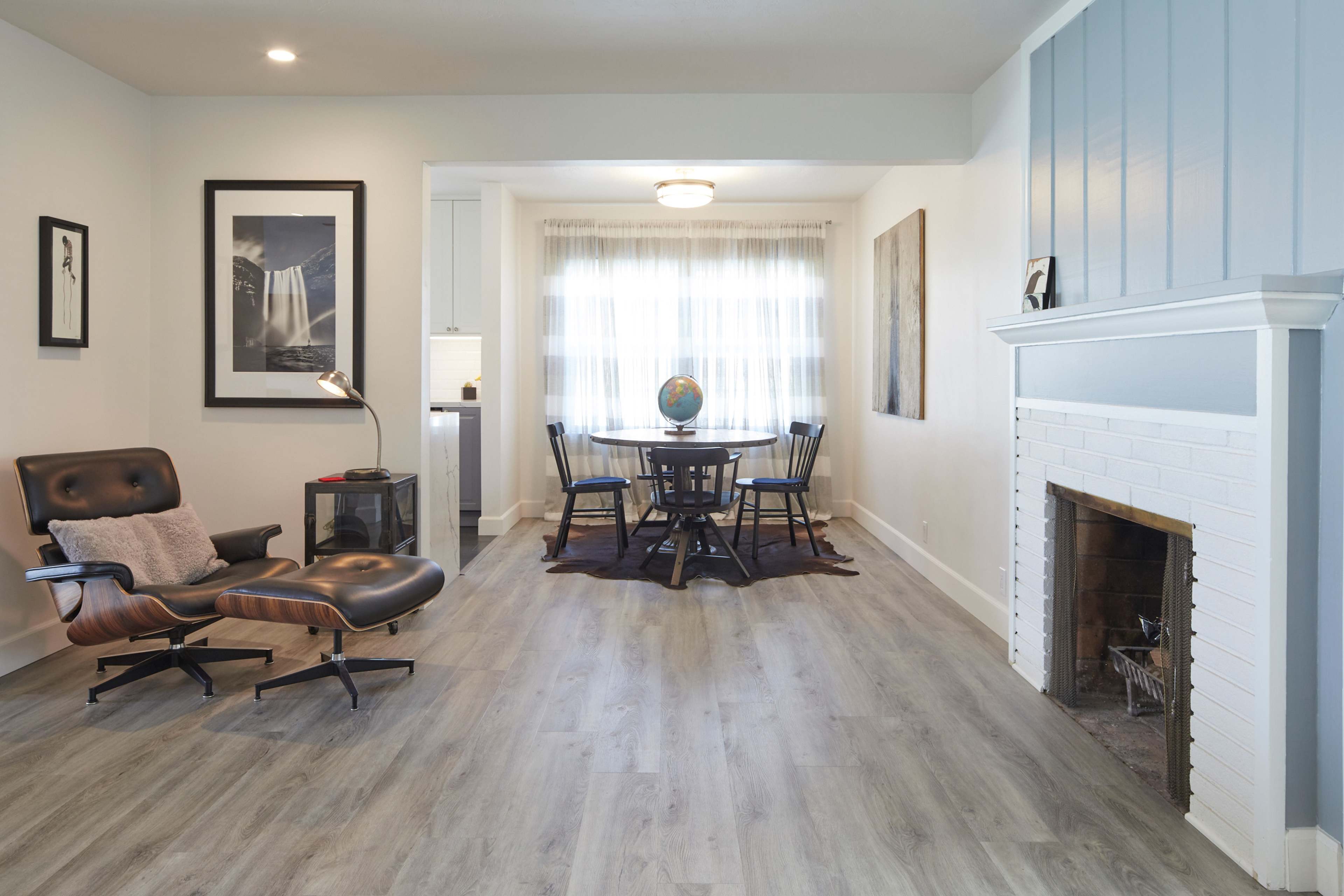 The image shows a modern living space featuring a black leather chair, a circular dining table with chairs, and a white brick fireplace.