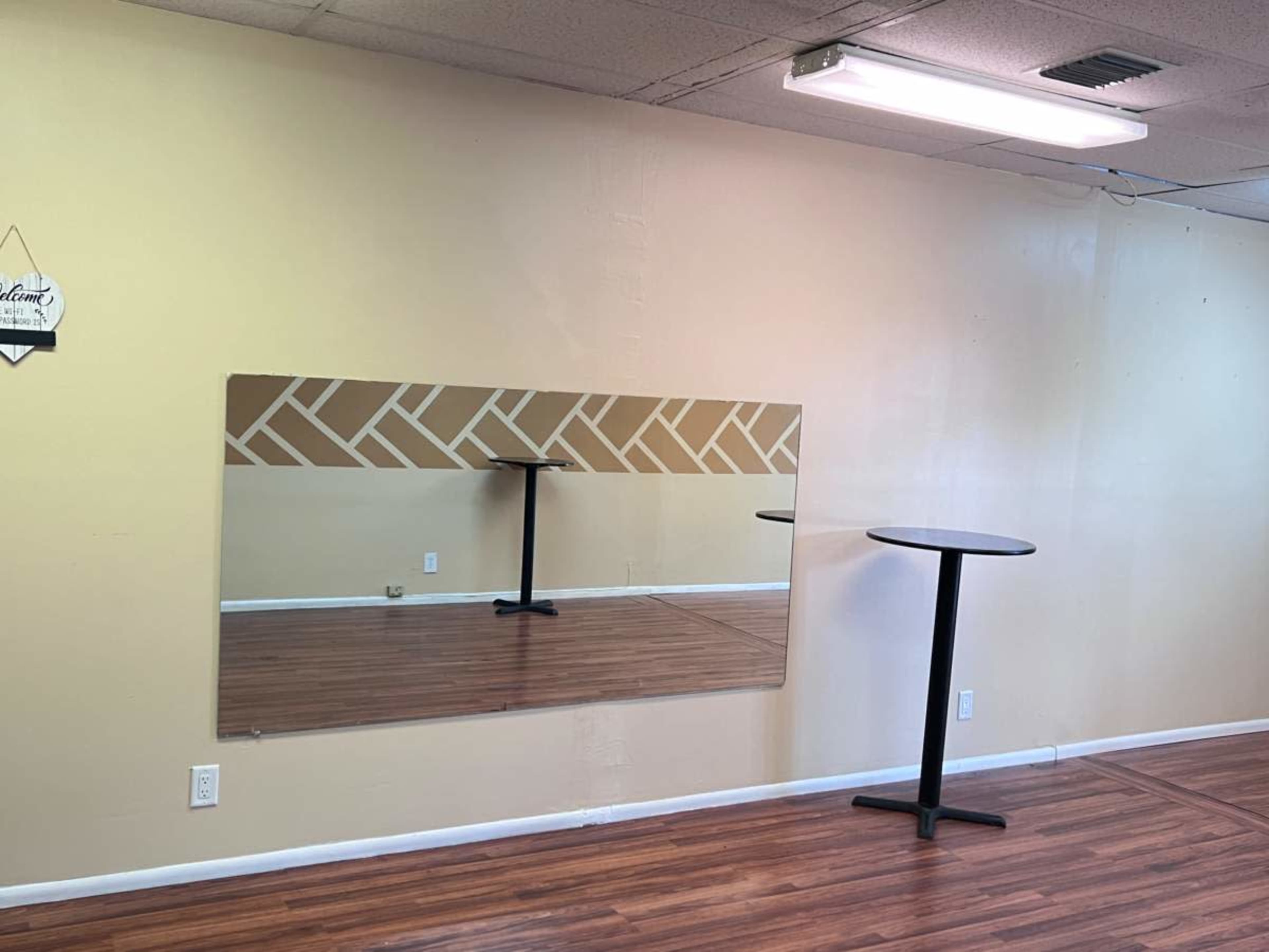 A wall with a large mirror and a small round table in an empty room with wooden flooring.