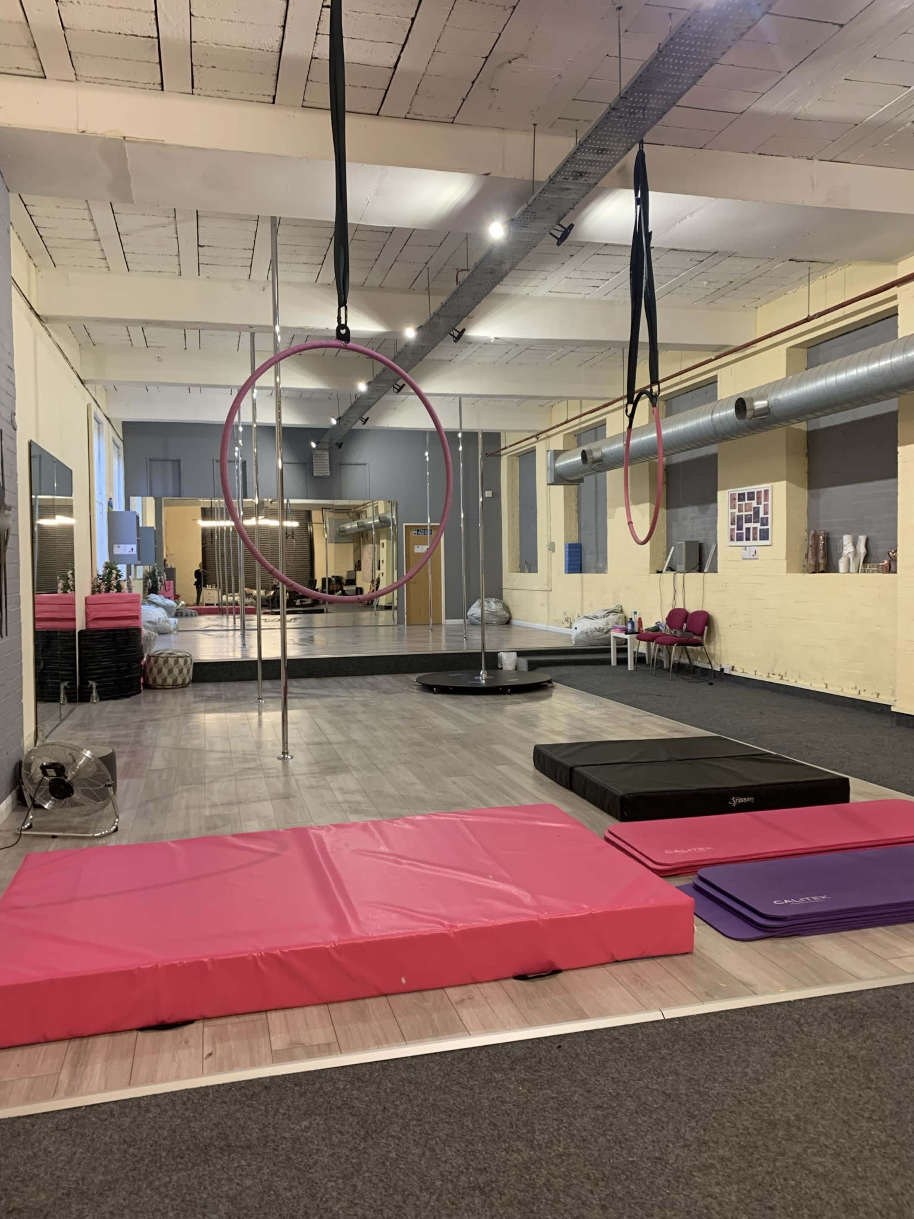 An indoor gym space featuring various exercise equipment, suspended hoops, and mats arranged on the floor.