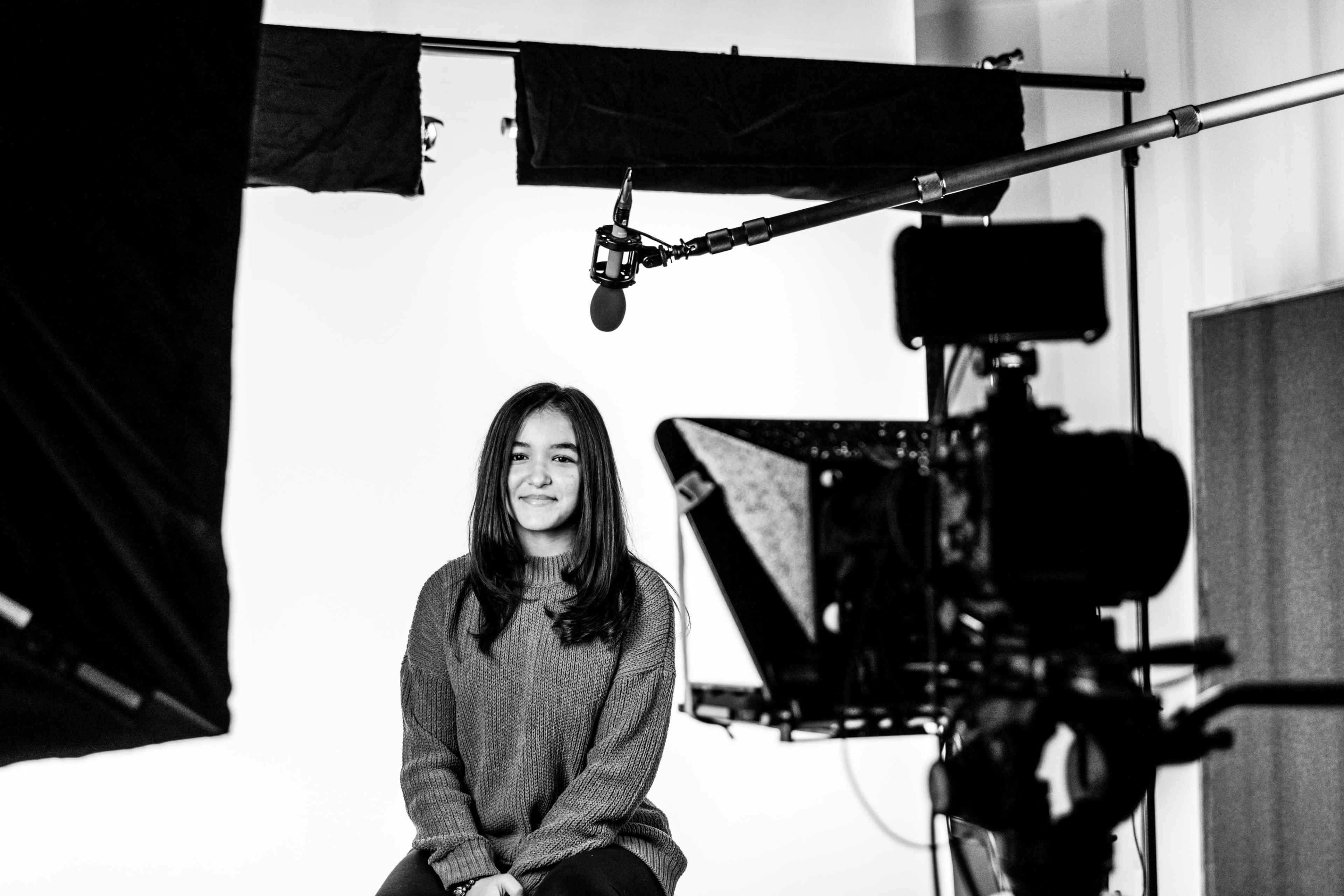 A woman sits in front of a camera and microphone setup in a brightly lit studio.