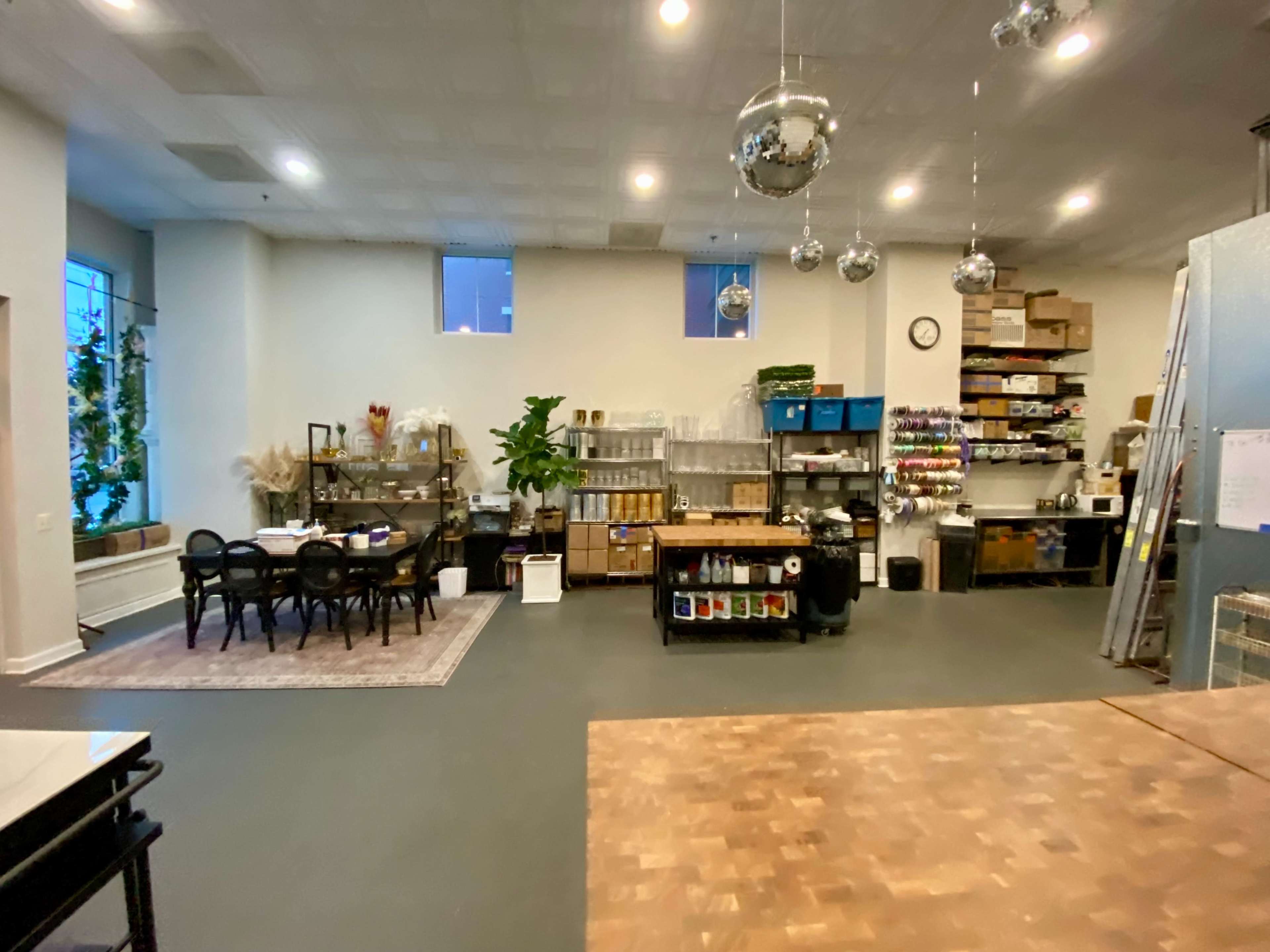 An industrial-style space with a dining area, shelving units, and various supplies stored on counters, along with hanging disco balls.