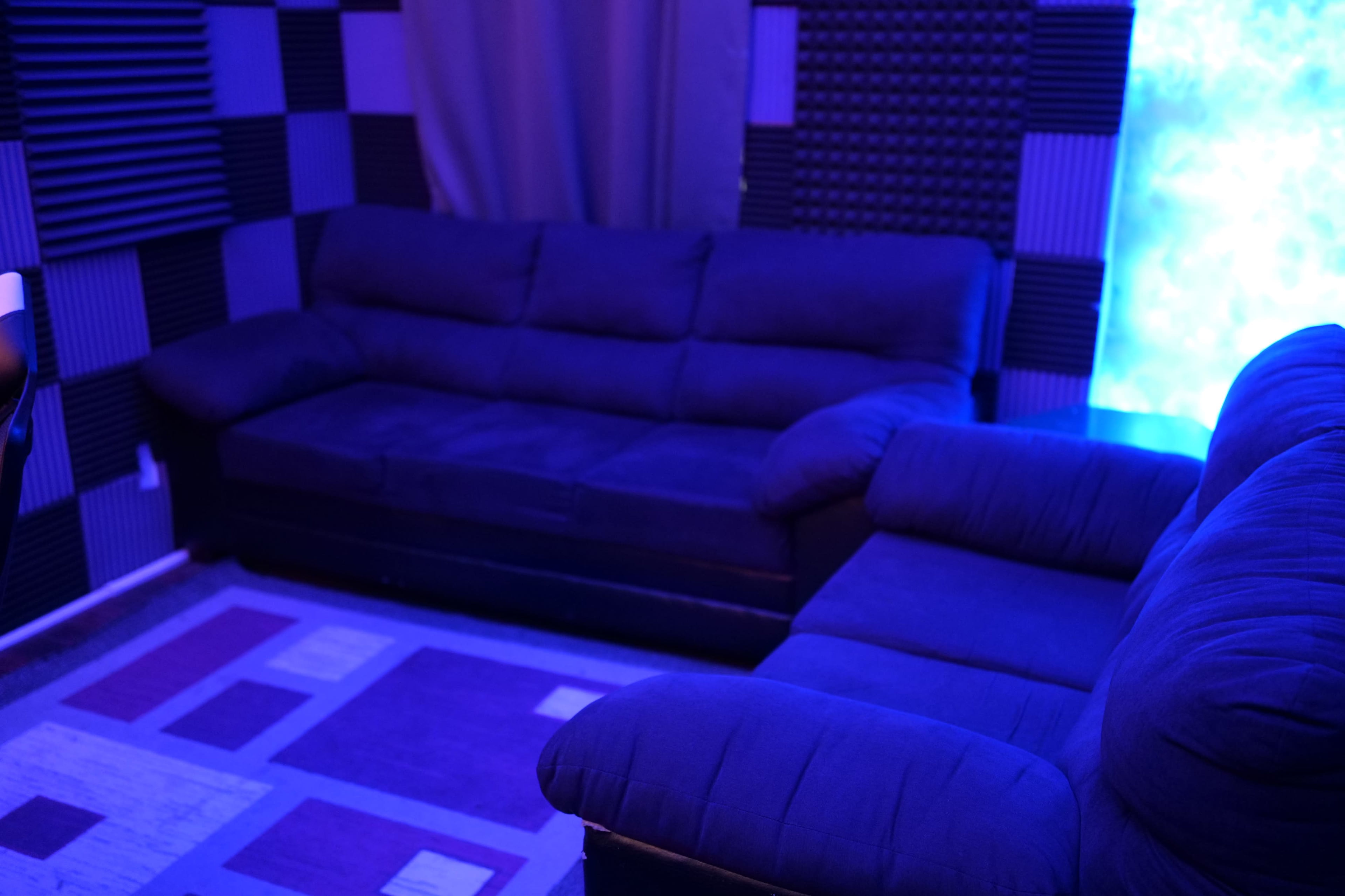A dimly lit room with a dark blue sectional couch and soundproofing panels on the walls.