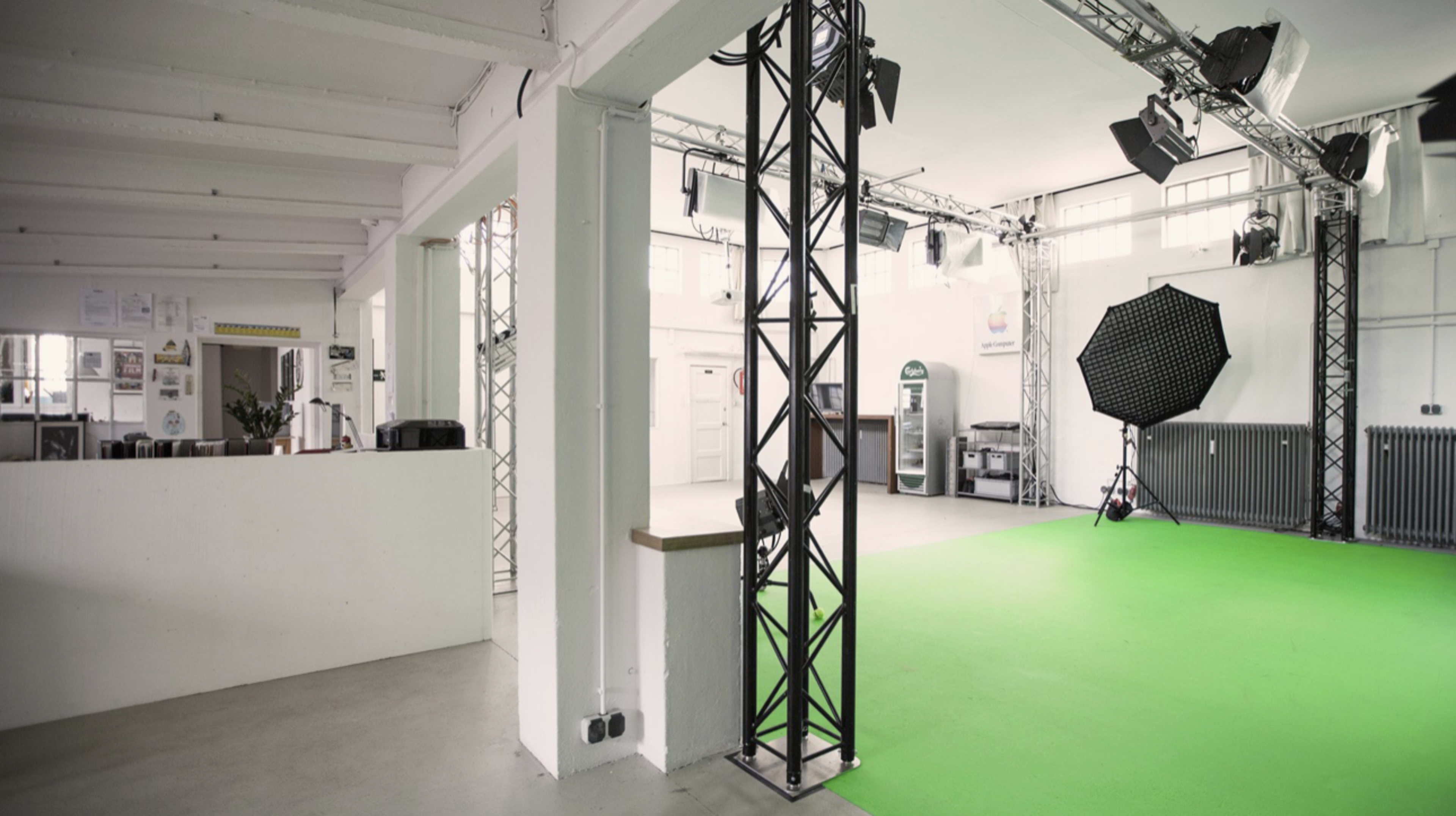 The image shows an empty studio space with a green backdrop, lighting equipment, and a minimalist design.
