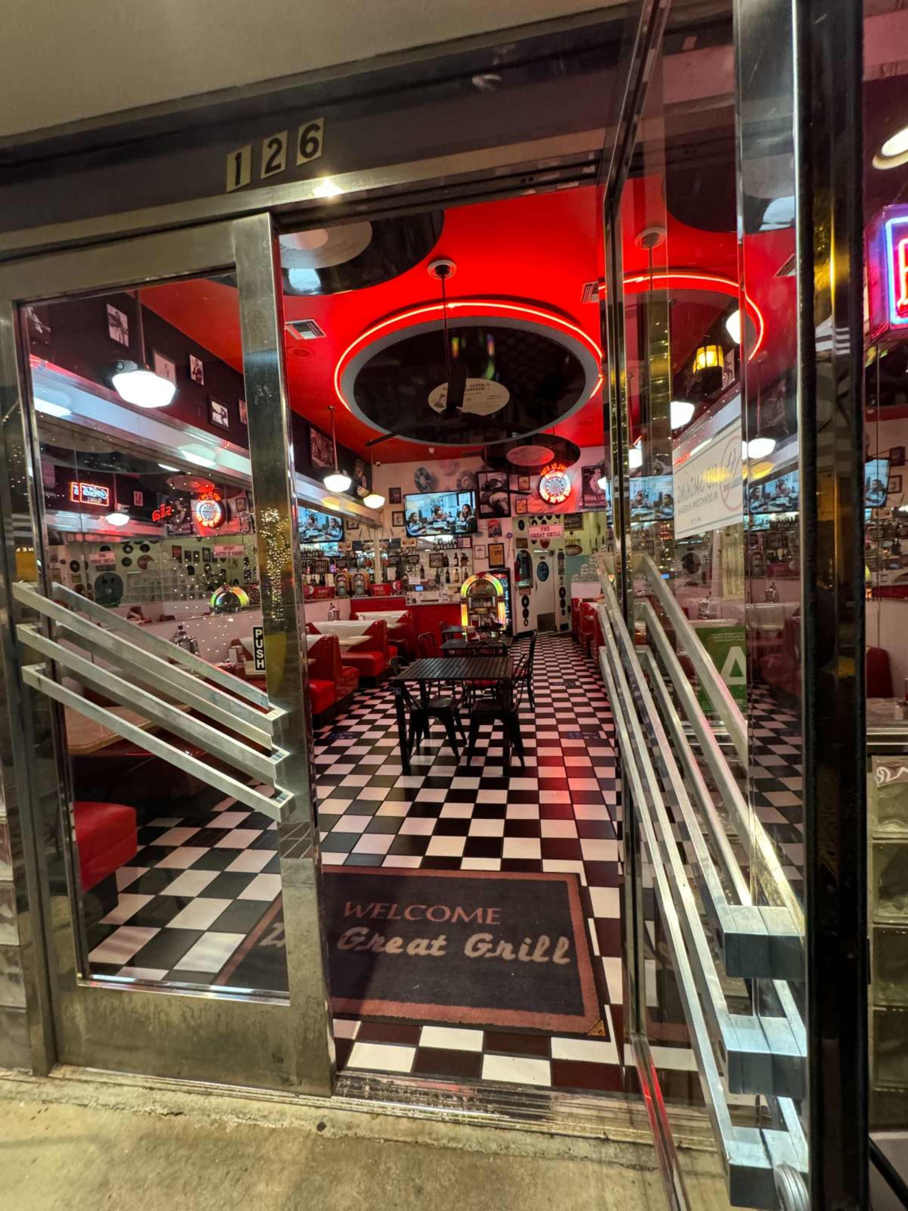 The entrance of a retro diner features red lighting, a checkered floor, and seating arranged around small tables.